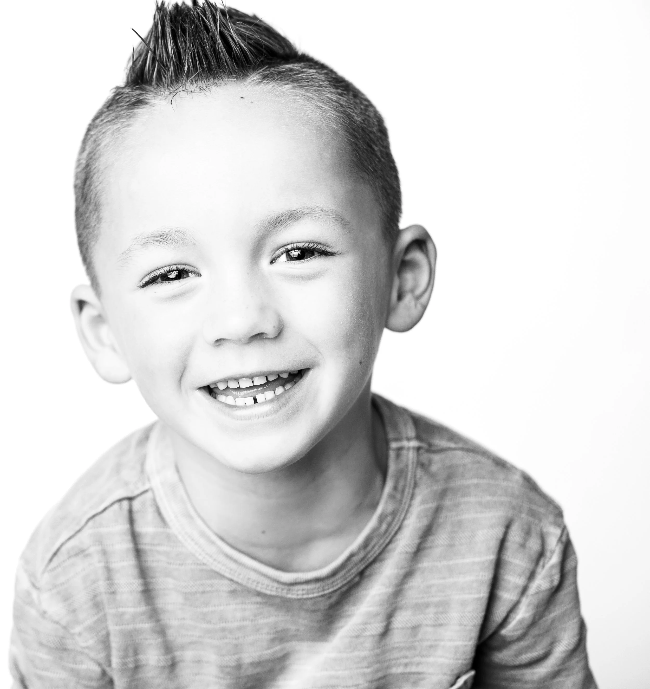 Smiling young boy with short, spiked hair wearing a striped T-shirt posed against a plain white background.