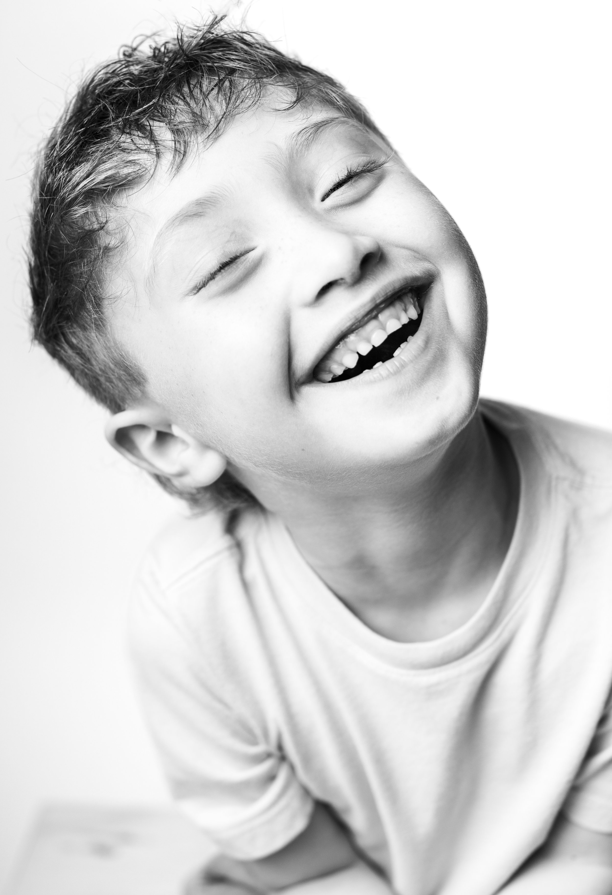Black and white photo of a young boy with a joyful expression, eyes closed, mouth open in a big smile, showing missing teeth.