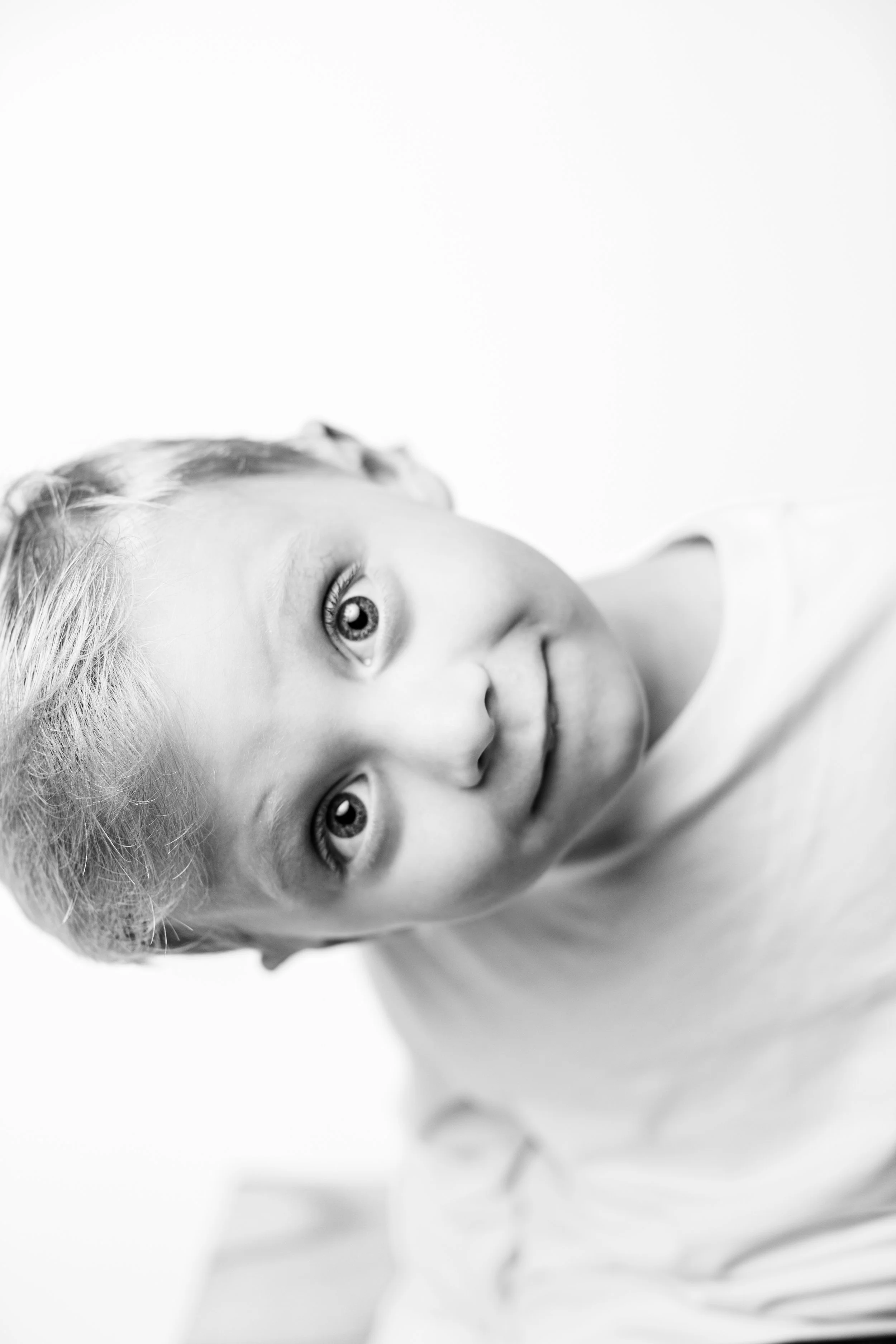 Black and white photo of a young girl lying on her side, looking up at the camera with a gentle smile.