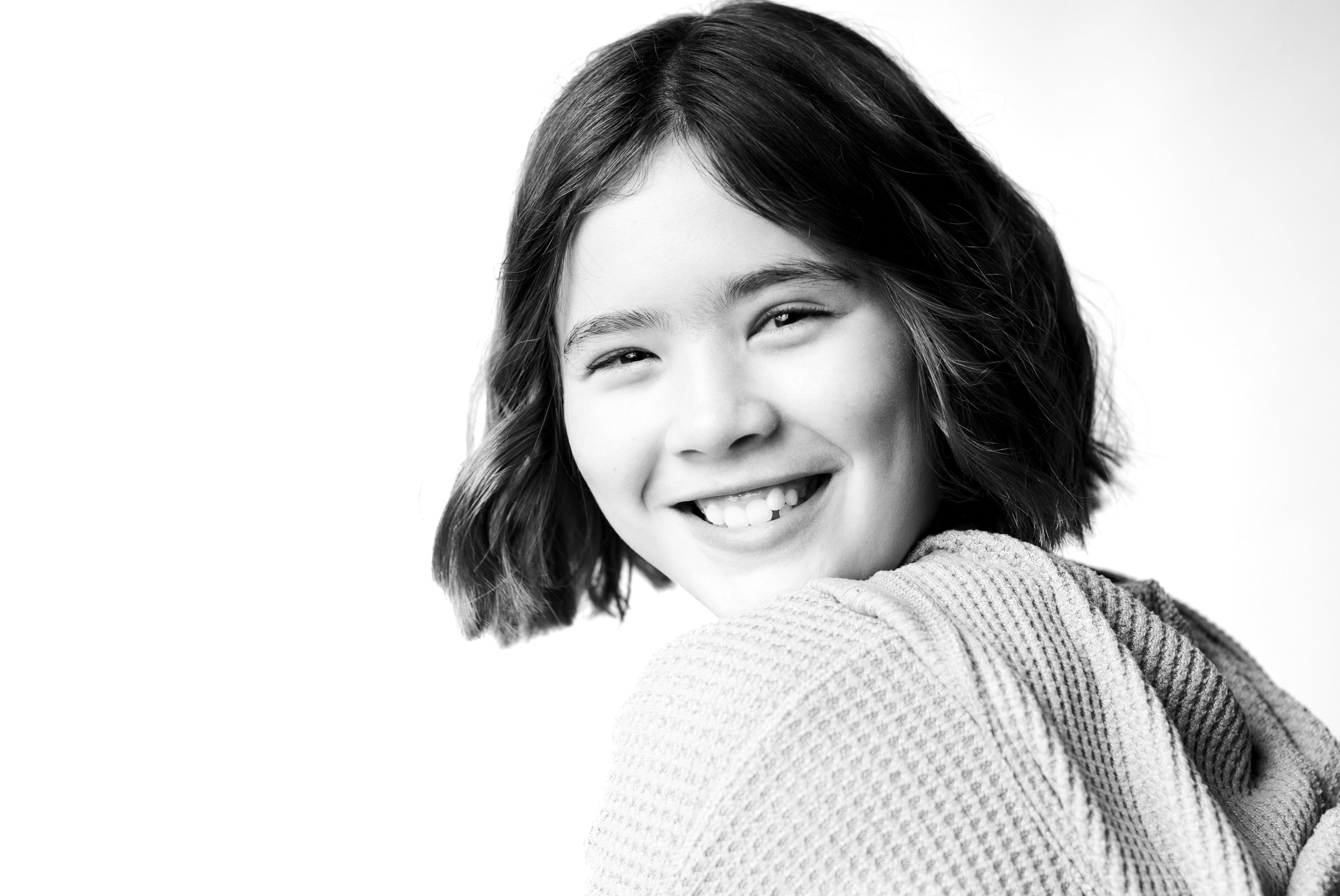 Black and white portrait of a young girl smiling and looking at the camera, with shoulder-length hair and a textured sweater.