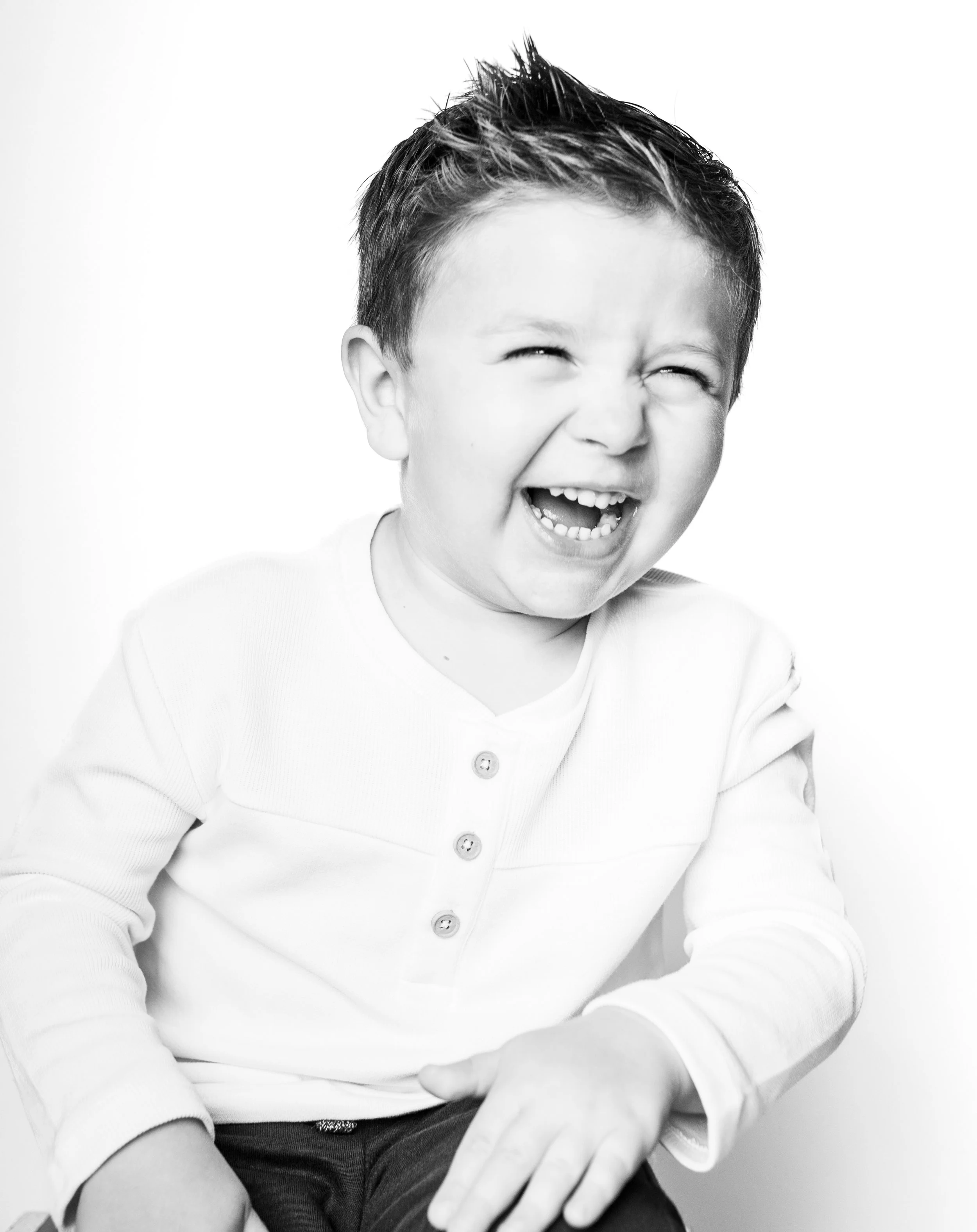 A young boy laughing with his eyes closed, wearing a long-sleeve shirt, on a white background.