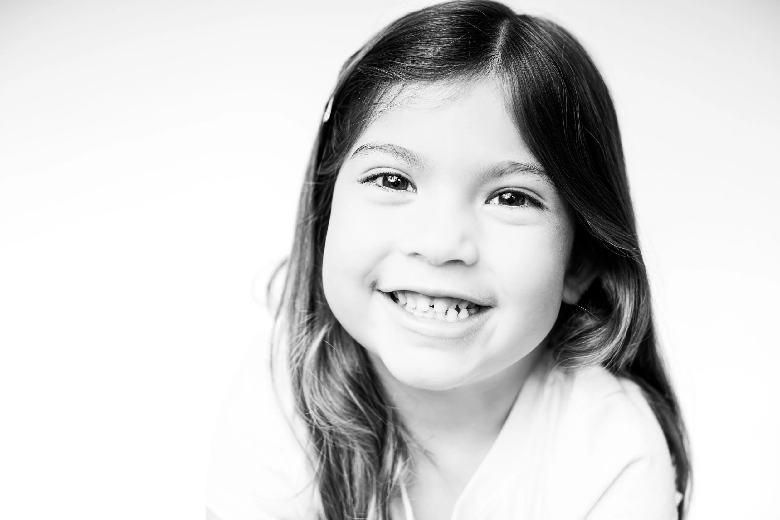 Black and white portrait of a young girl with long hair smiling showing her teeth.