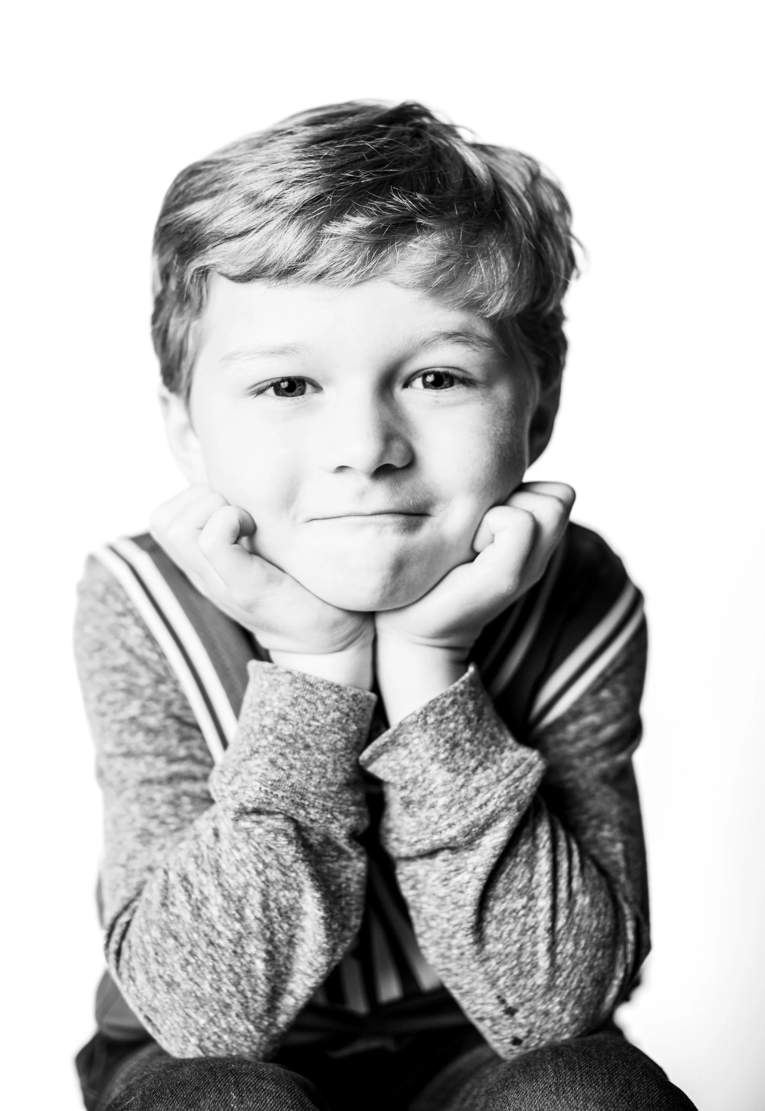 Child resting chin on hands, leaning forward, smiling, black-and-white portrait.