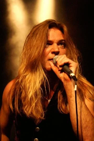 Tracie Law, singer with Symphony of Pain, with long blonde hair singing into a microphone under stage lighting.