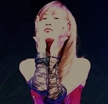 Cellist, Jiaxin Lloyd Webber with long hair and bangs, posing with her hands on her face, wearing lace gloves and a red dress against a dark background as part of the video shoot for the Symphony of Pain track 'Suspicion'.