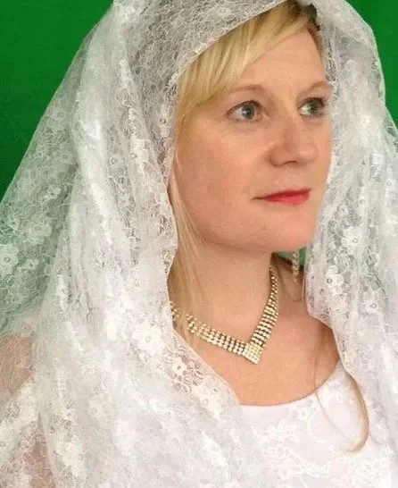 A woman with blonde hair wearing a white lace veil and a pearl necklace, against a green background. This is part of a video shoot for the band Symphony of Pain's song, Kiss the Bride. 