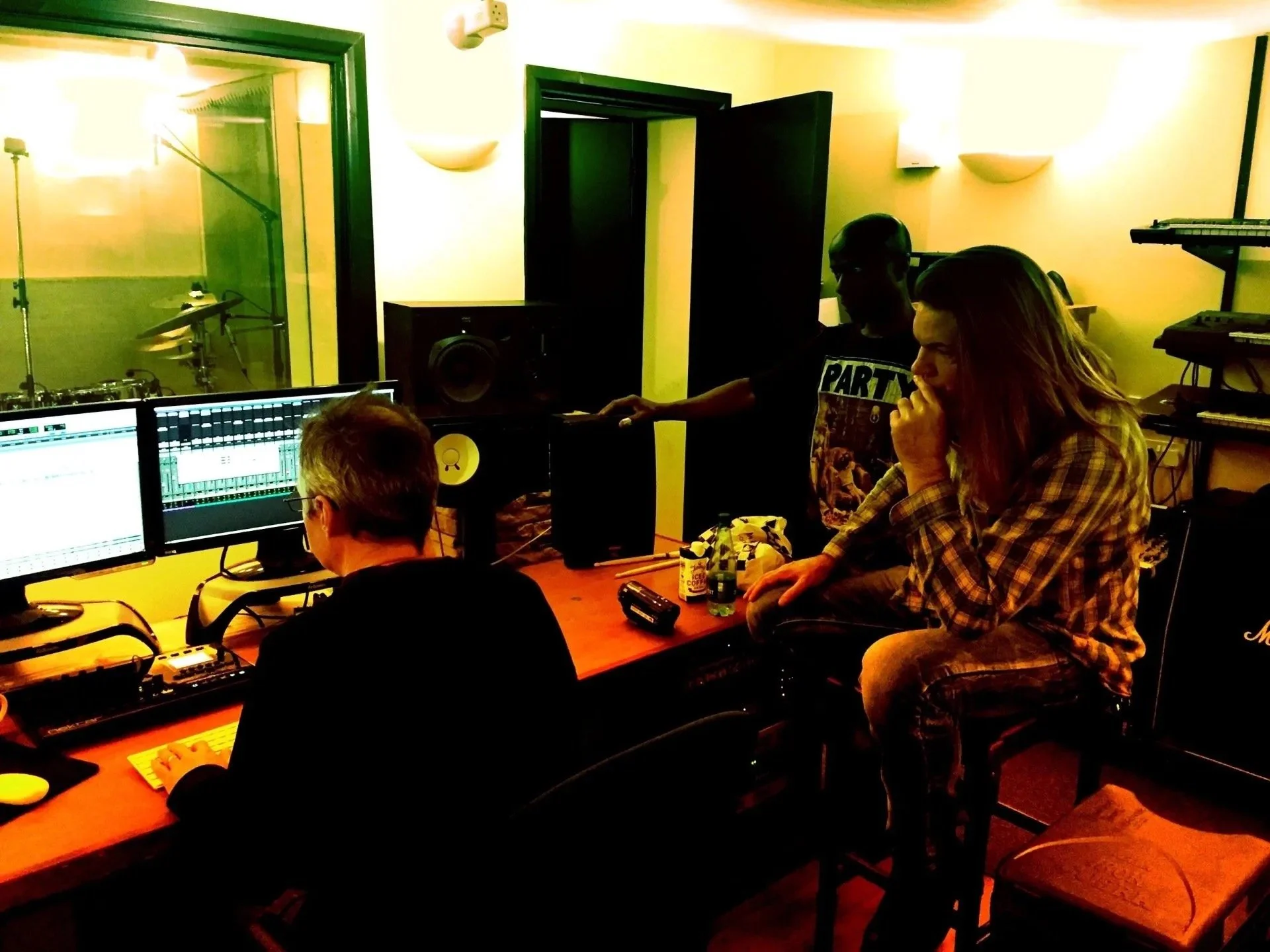 Thin Ice music recording studio with four people sitting in it, recording Symphony of Pain 'Virology'. One person working at a computer with audio editing software, two people observing, and one person in the background near musical equipment.