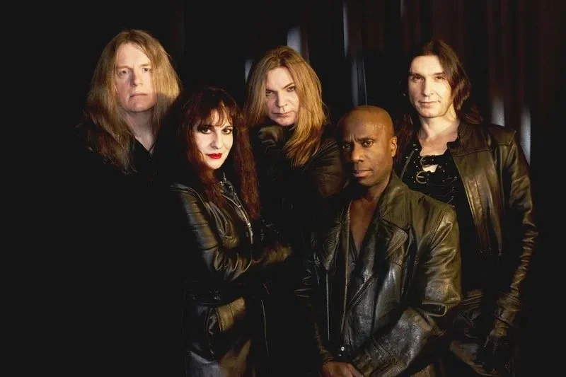 The musicians from the band Symphony of Pain, Tracie Law, Pam Chowhan, Johanne James, Mark Bloxsidge and Jonas Costa posing with serious expressions, all wearing black leather jackets, against a dark background.