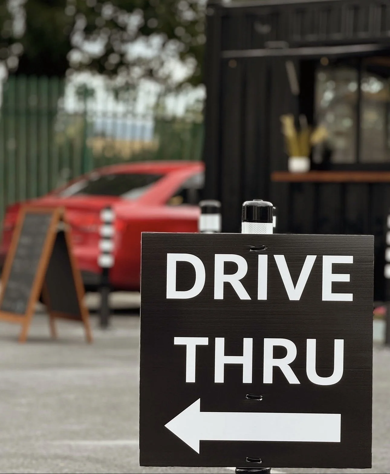 A black and white sign that says "Drive Thru" with an arrow pointing to the left, outside of a fast-food or restaurant establishment.
