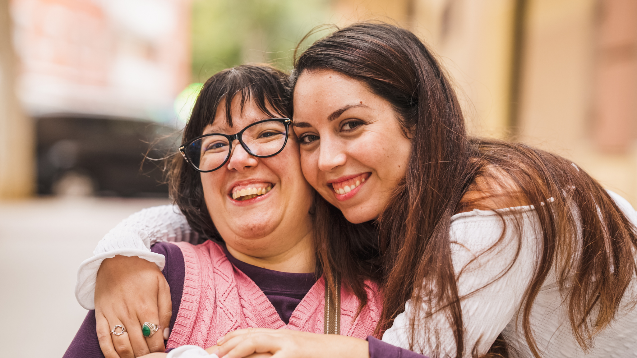 Two women hugging and smiling warmly at the camera.