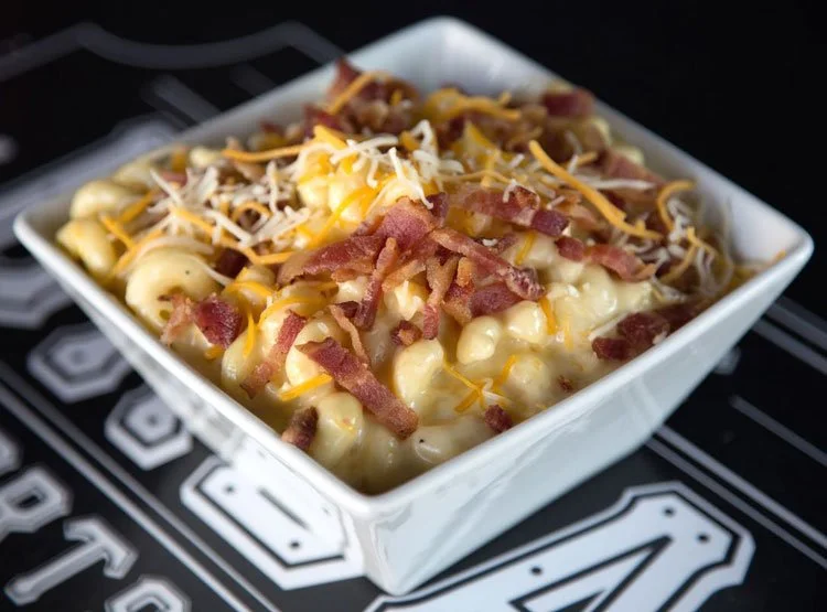 Bowl of macaroni and cheese topped with shredded cheddar and mozzarella cheese, bacon bits, and grated cheese.