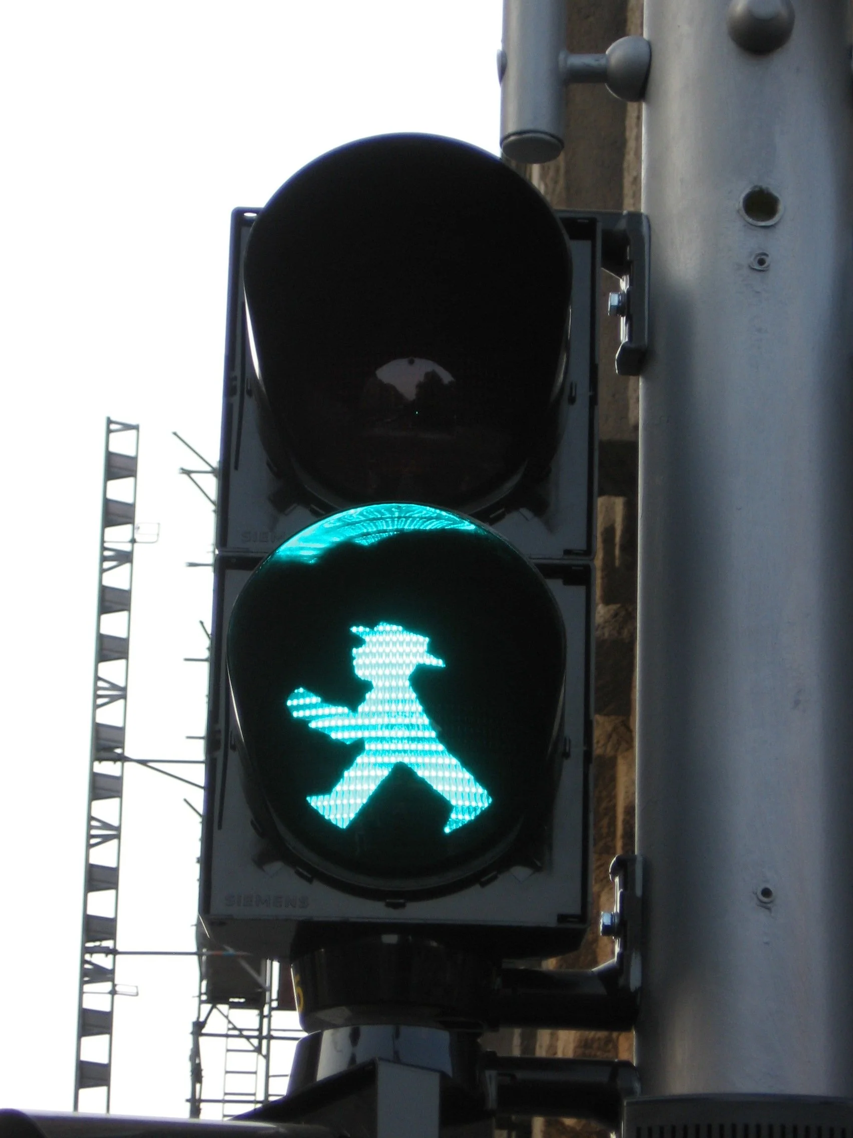 Sinal de trânsito de pedestre iluminado com luz verde, mostrando uma silhueta de pessoa caminhando. Berlim, setor oriental.