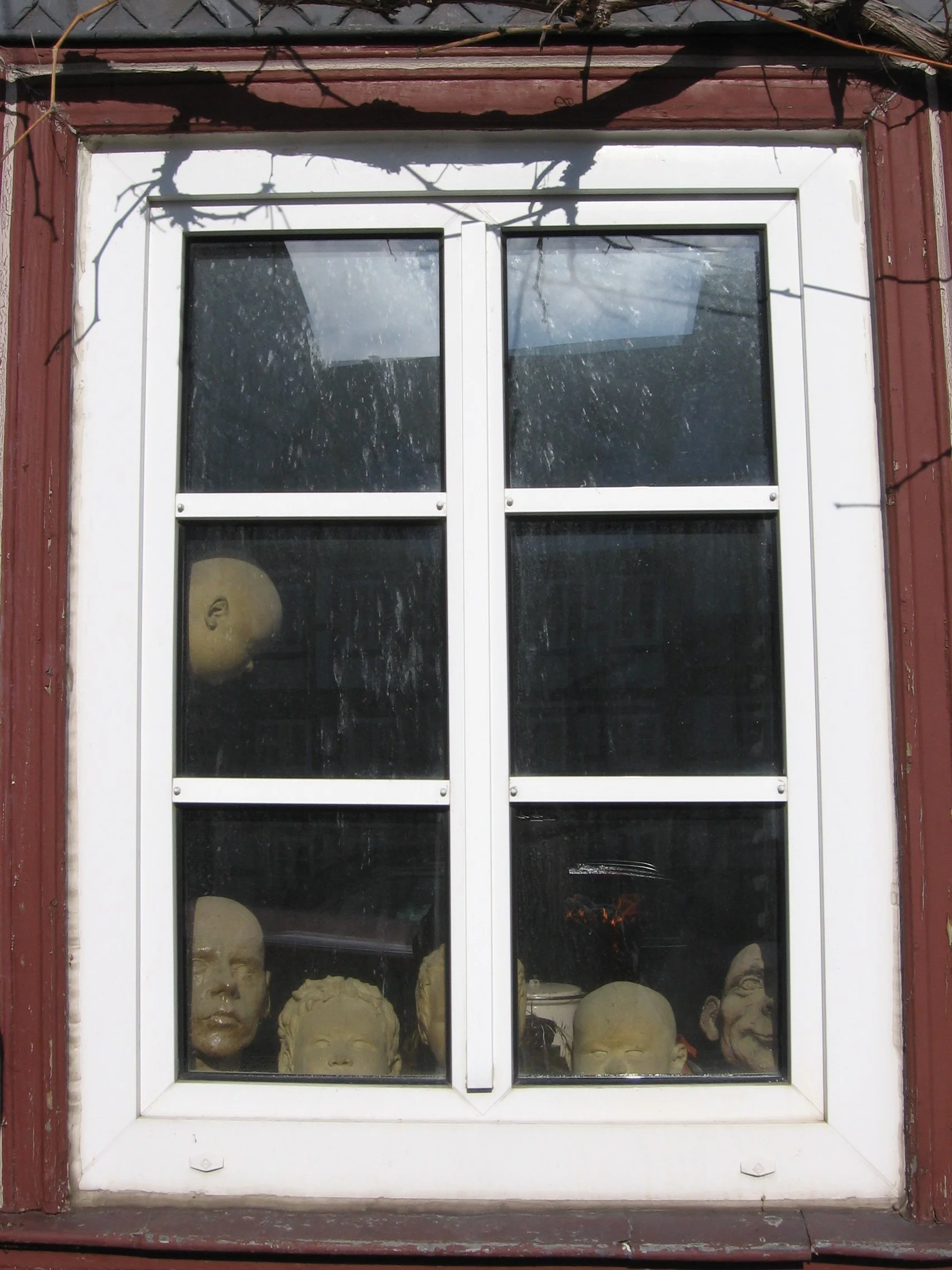 Janelas com vidros sujos e bonitas cabeças de comédia e teatro, provavelmente máscaras de teatro, dentro de uma caixa de vidro na parede de uma casa ou teatro. Goslar, Alemanha.