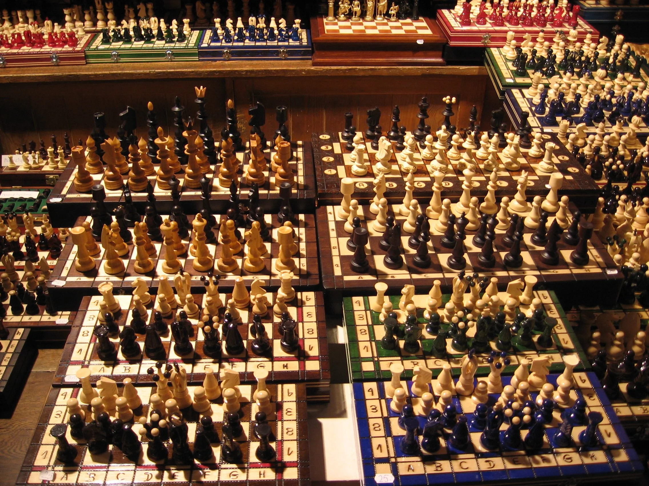 Várias tabuleiros de xadrez com peças de diferentes cores, símbolos e tamanhos, em uma mesa de madeira. Lojinha do mercado perto da praça principal de Cracóvia, Polônia. 