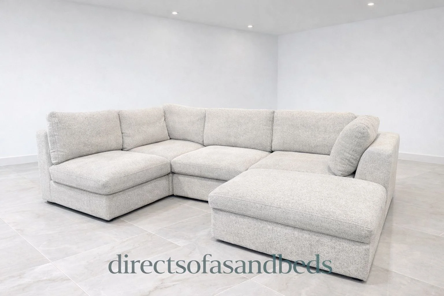 Light gray sectional sofa with cushions in a minimalistic room with white walls and tiled flooring.