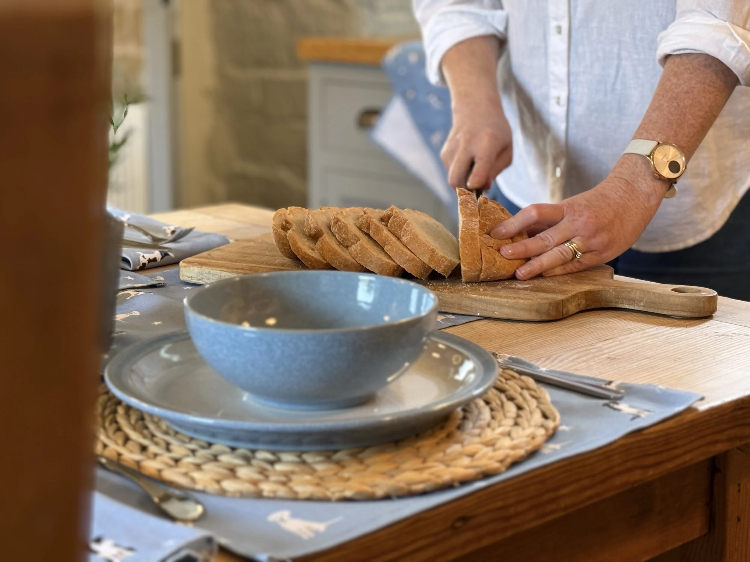 Person slicing a loaf of bread on a wooden cutting board in a kitchen setting.