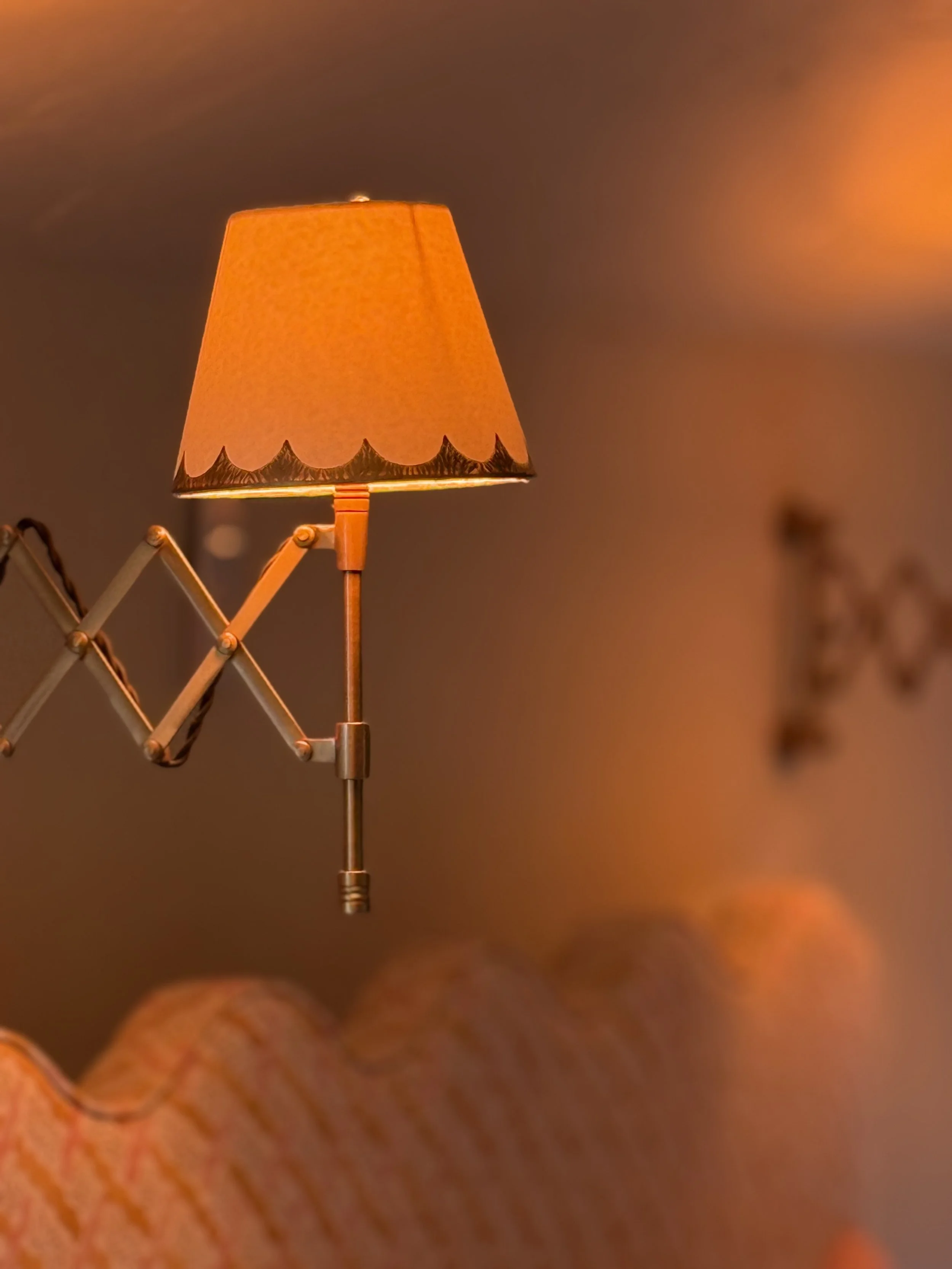 Close-up of a vintage wall-mounted lamp with a yellow-orange lampshade emitting warm light, next to a patterned sofa.