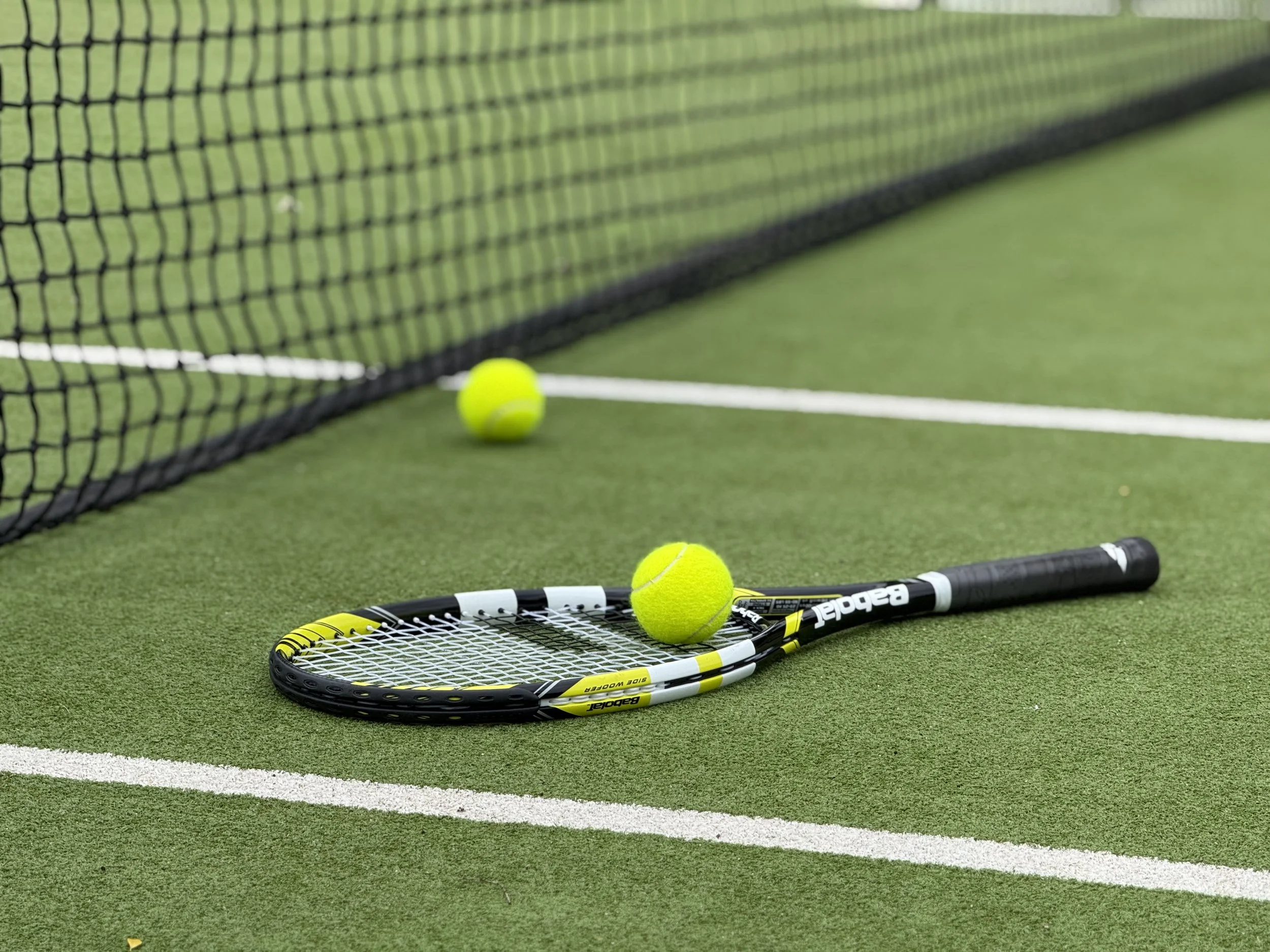 Tennis ball and tennis racket on a green tennis court near the net.