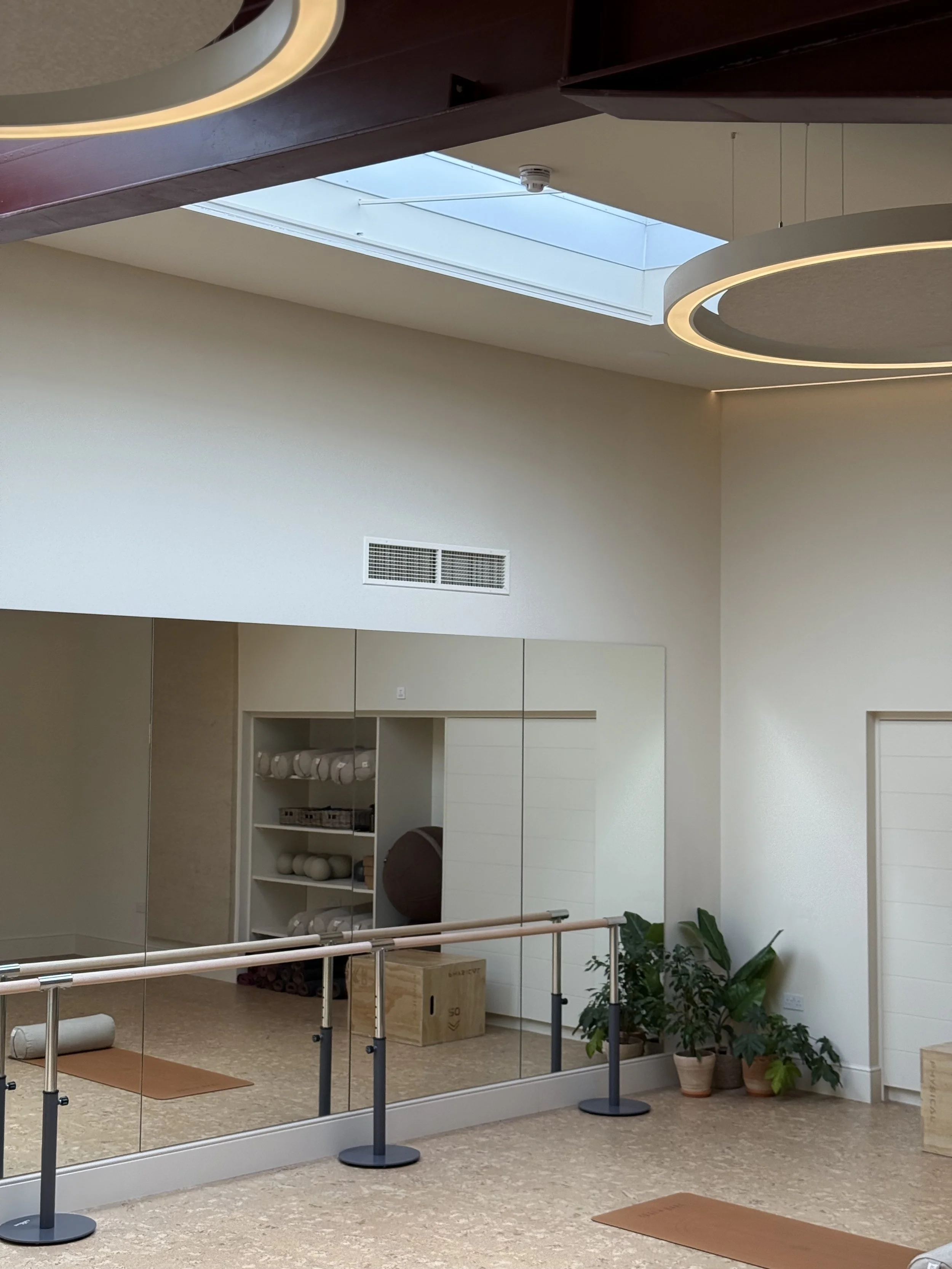 A yoga studio with a mirror wall, plants, and yoga props like mats, blocks, and rollers, under a skylight.