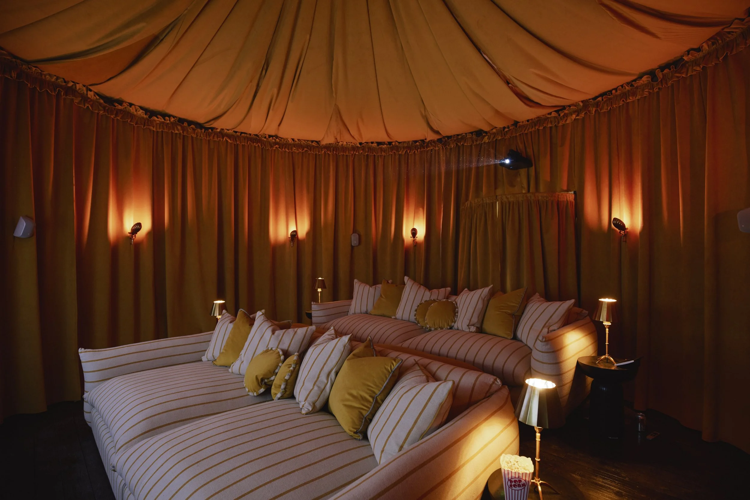 A cozy theater room with striped couches and yellow pillows, surrounded by warm orange curtains and soft lighting.