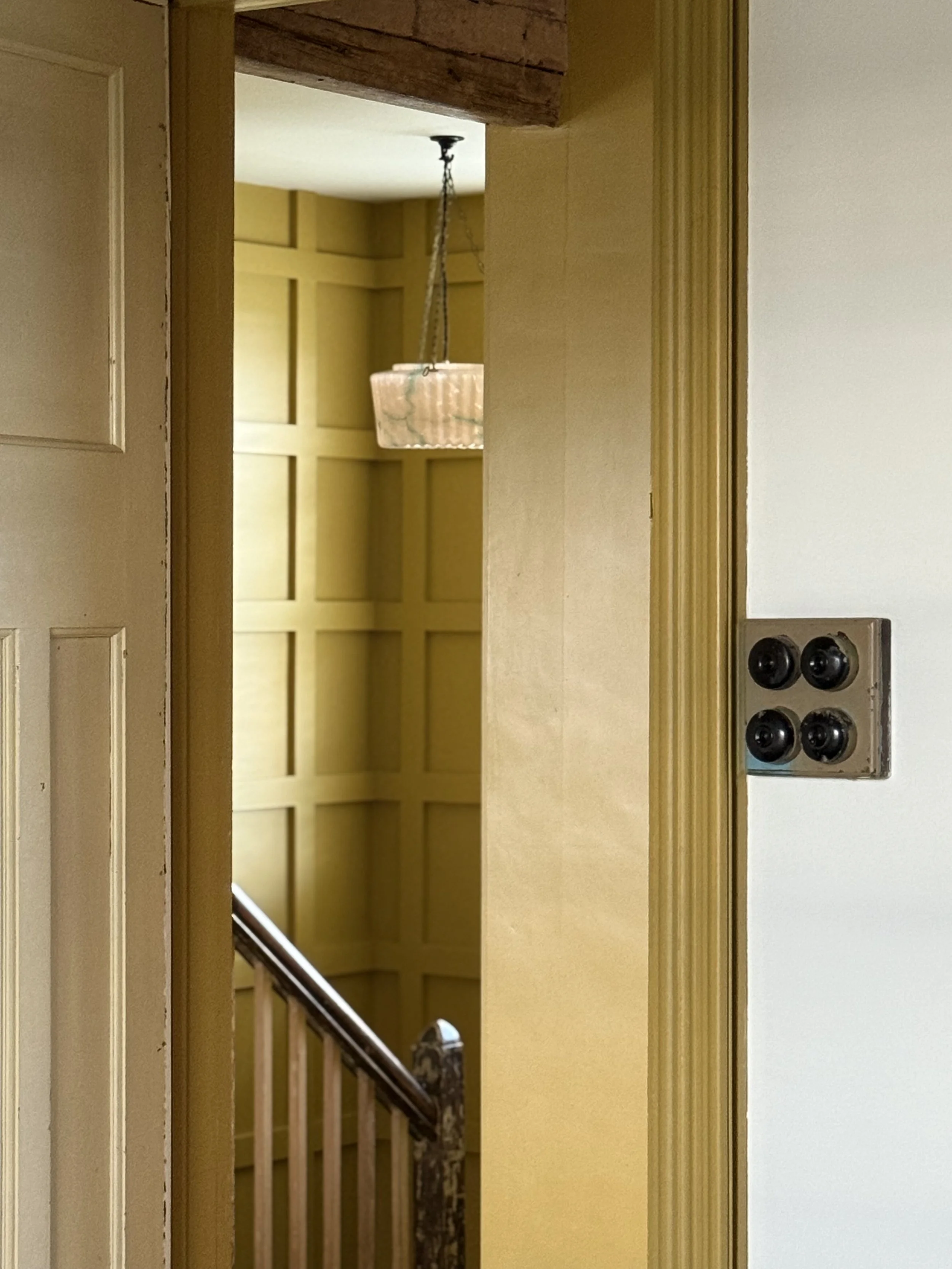 View of a staircase through an open doorway, with a yellow wall and a hanging light fixture visible in the background.