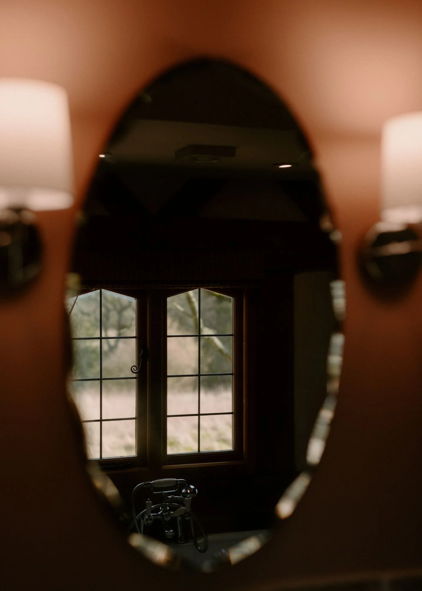 Photo of a home interior taken through an oval mirror, showing a window with trees outside and a bathtub below it.