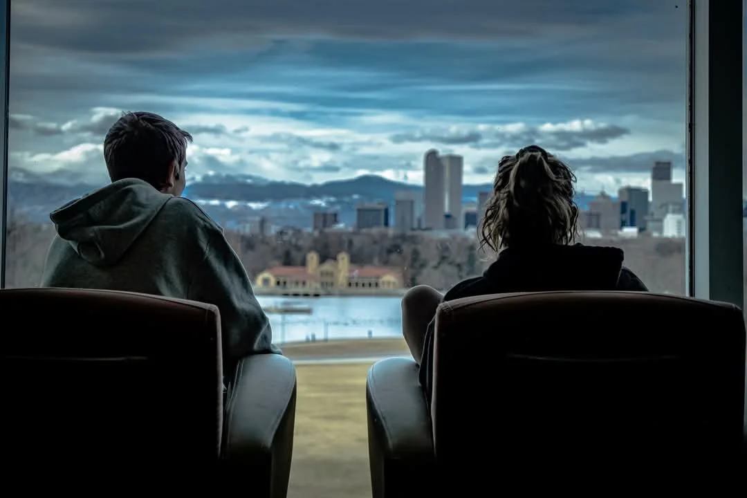 Image of Kathryn and her brother, Logan, sitting inside of the Denver Science and History Museum, looking at the Denver skyline. Image taken by Leigh Skonning.