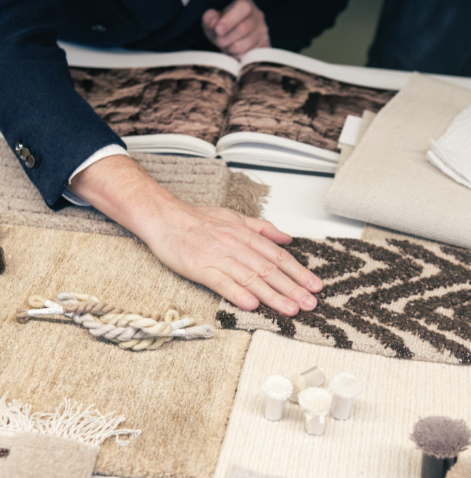 Person examining fabric and carpet samples on a table, with a catalog open in the background.