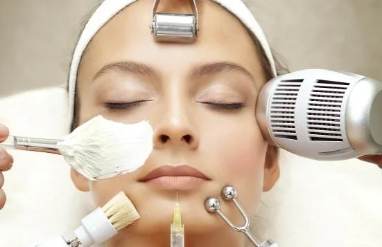 Girl receiving facial treatment with various skincare tools and devices around her face.
