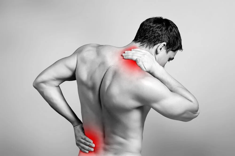 A shirtless man with black hair holds his neck and lower back, both areas highlighted in red to indicate pain.