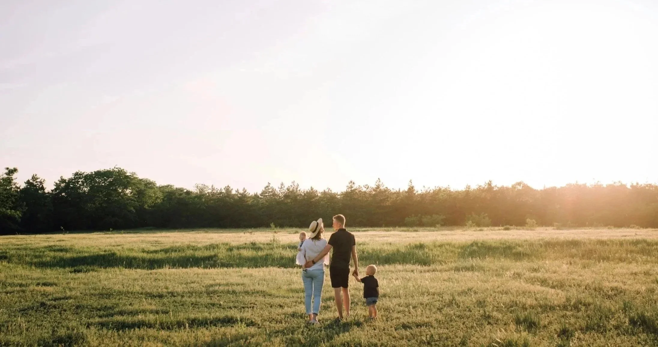 Family walking in a grassy field during sunset, with trees in the background.