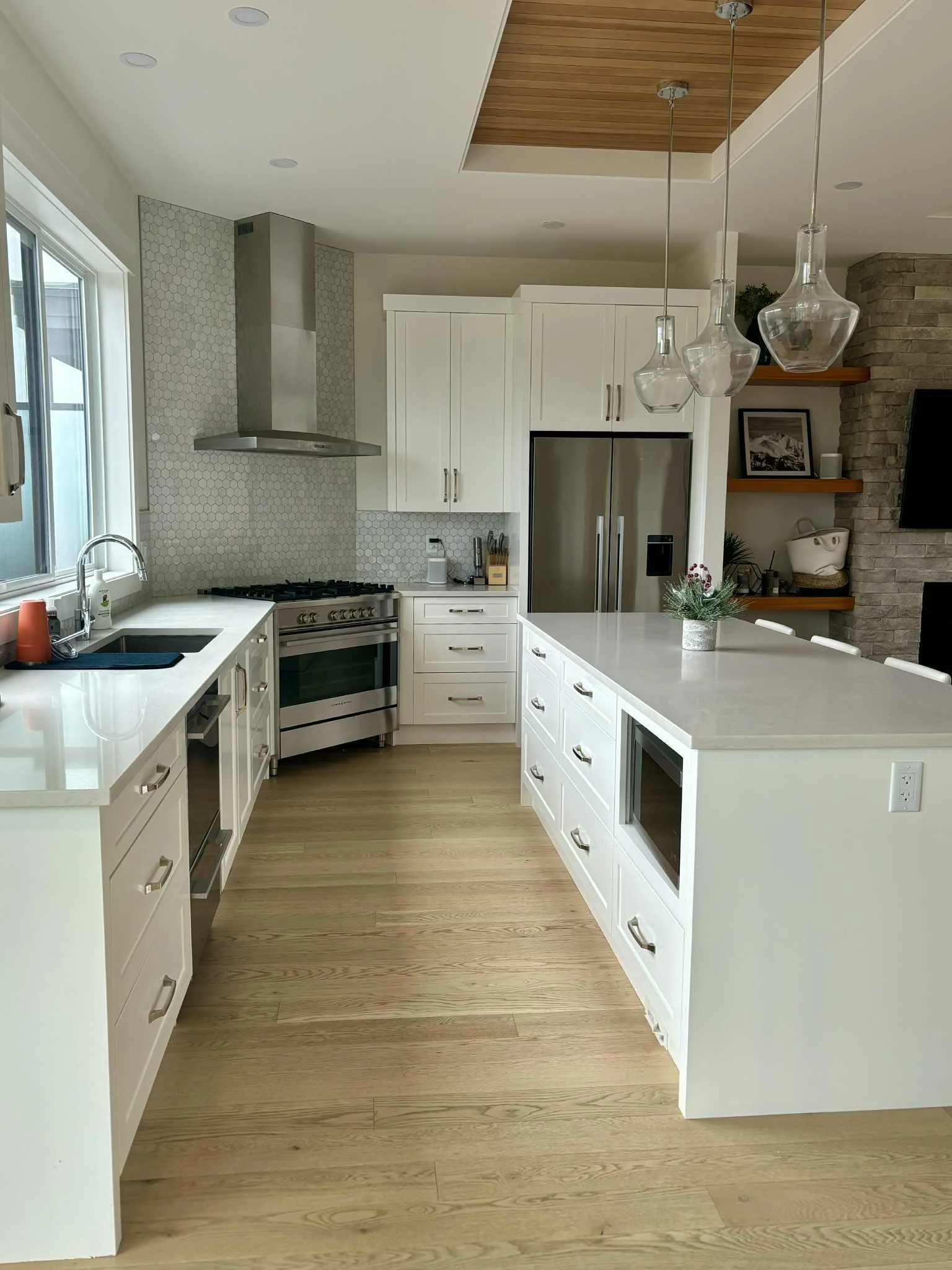 Modern white kitchen with wood flooring, stainless steel appliances, and a kitchen island with a flower arrangement.
