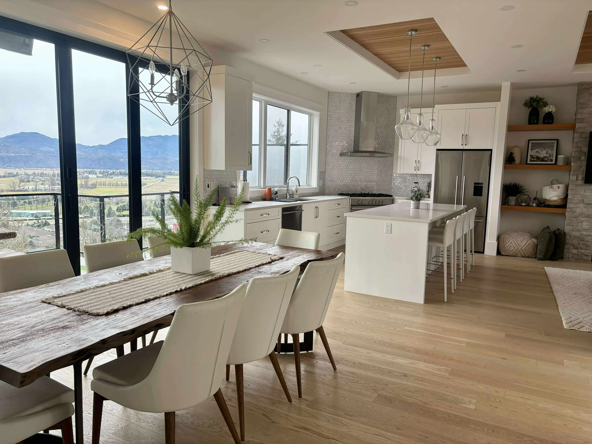Open-concept kitchen and dining area with hardwood floors, white cabinetry, large windows, mountain view, and modern decor.