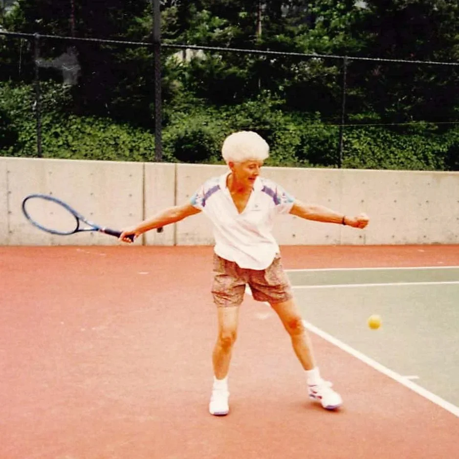 An elderly woman with white hair playing tennis on a court.