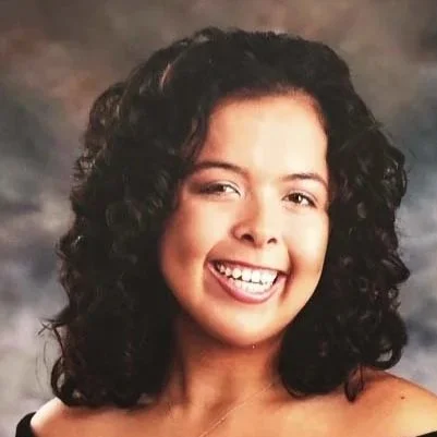 A young woman with curly dark hair smiling at the camera.