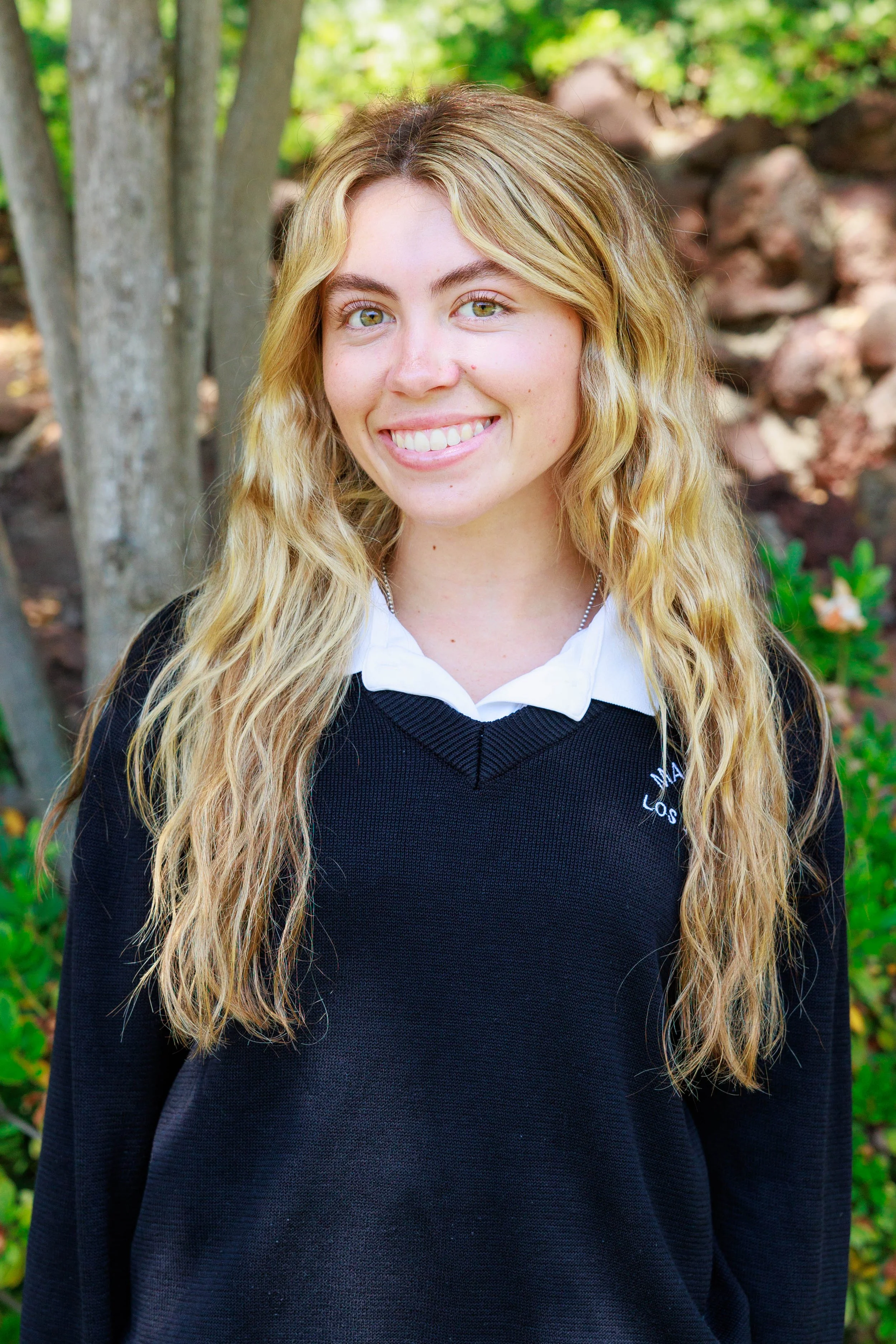 Portrait of a young woman with long brown hair smiling, wearing a black top and a necklace.