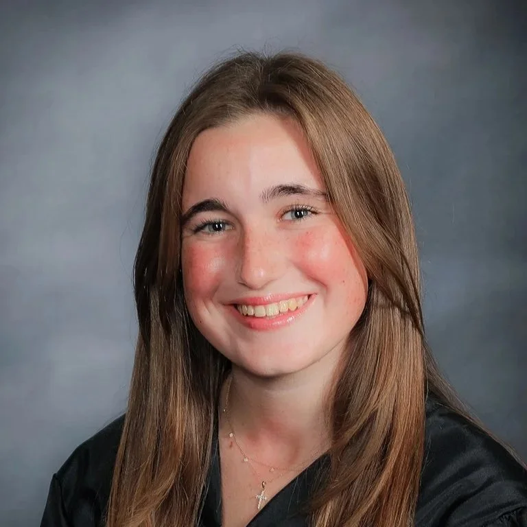 Portrait of a young woman with long brown hair smiling, wearing a black top and a necklace.