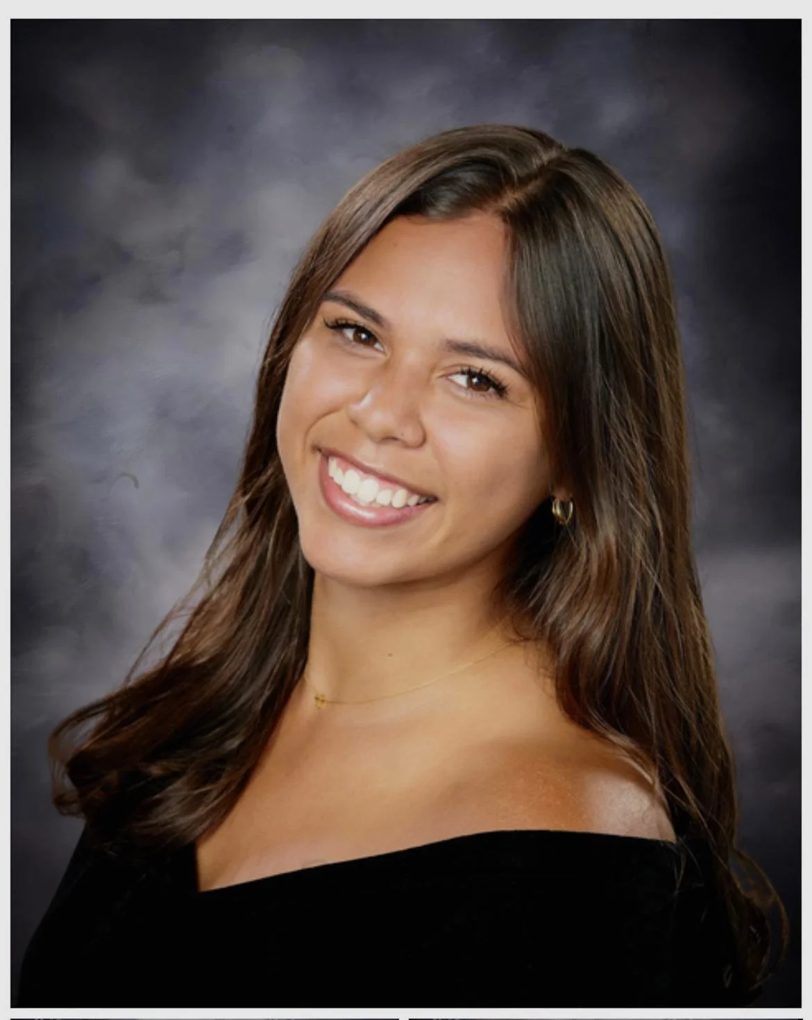 A young woman with long dark hair smiling at the camera against a plain light-colored background.