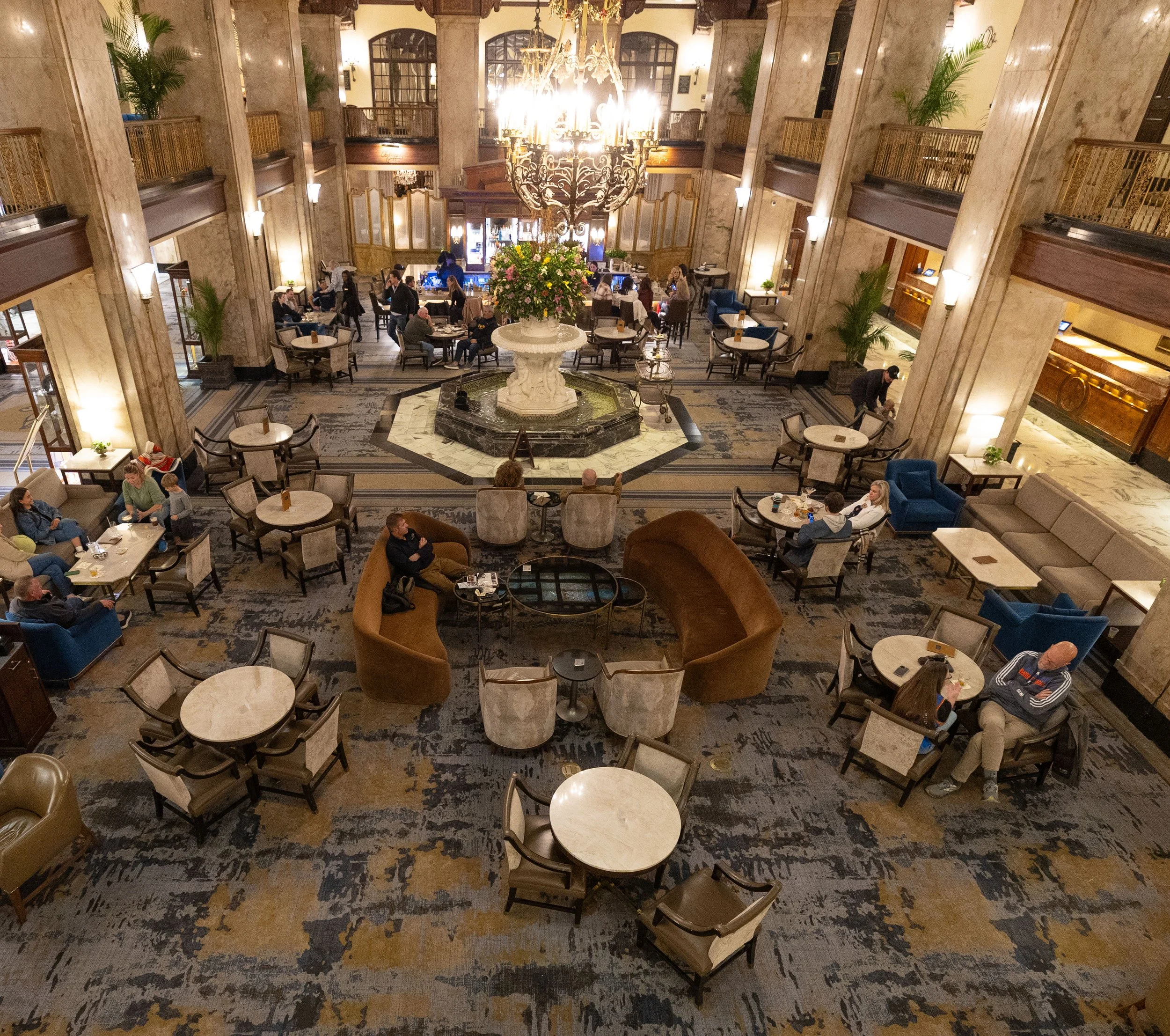A hotel lobby with a high ceiling, large chandelier, and a marble fountain with flowers in the center. Peabody Hotel Memphis.