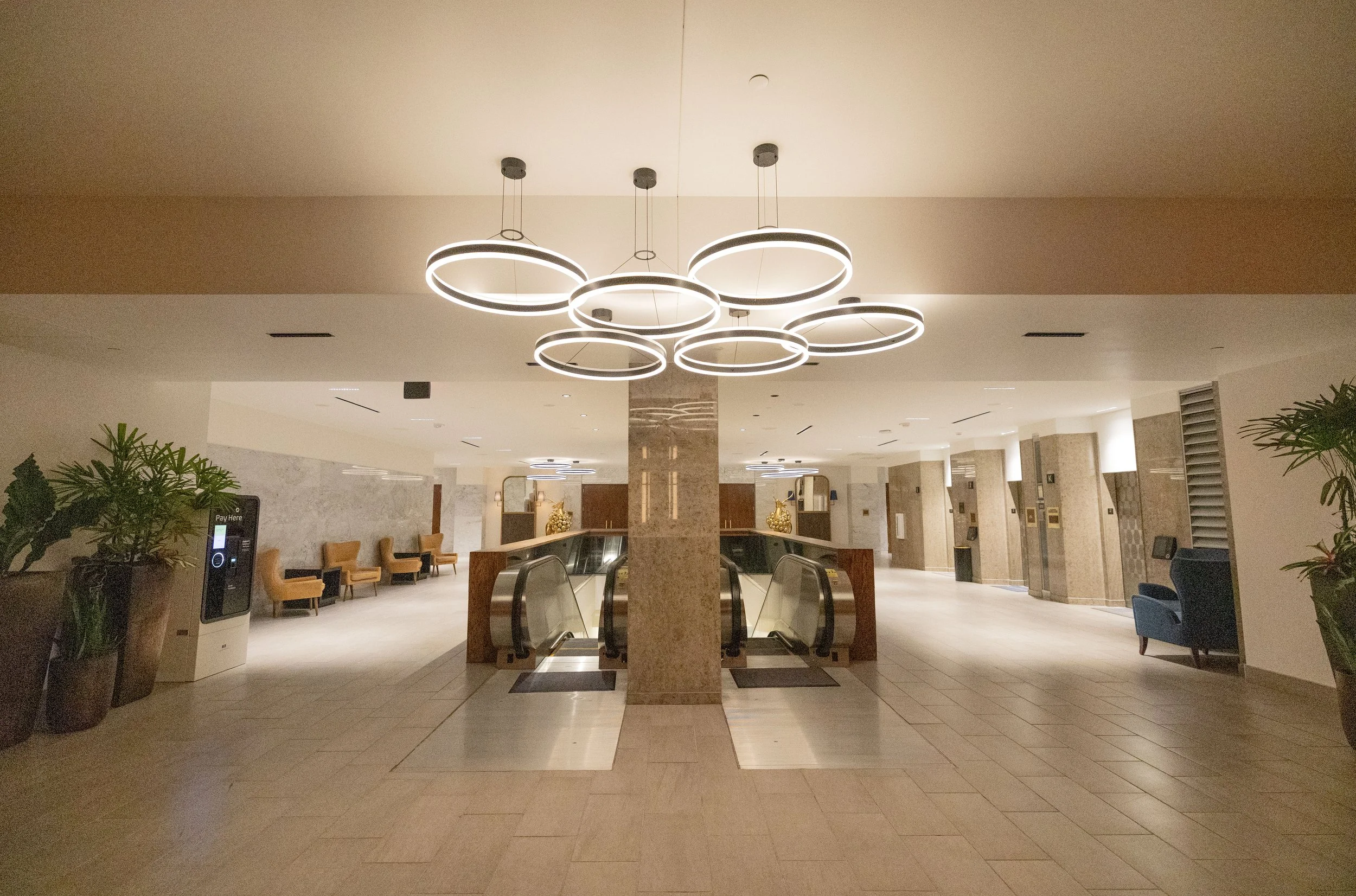 Open hotel lobby with seating, plants, escalators, and modern circular ceiling lights.  The National Hotel, Oklahoma City.