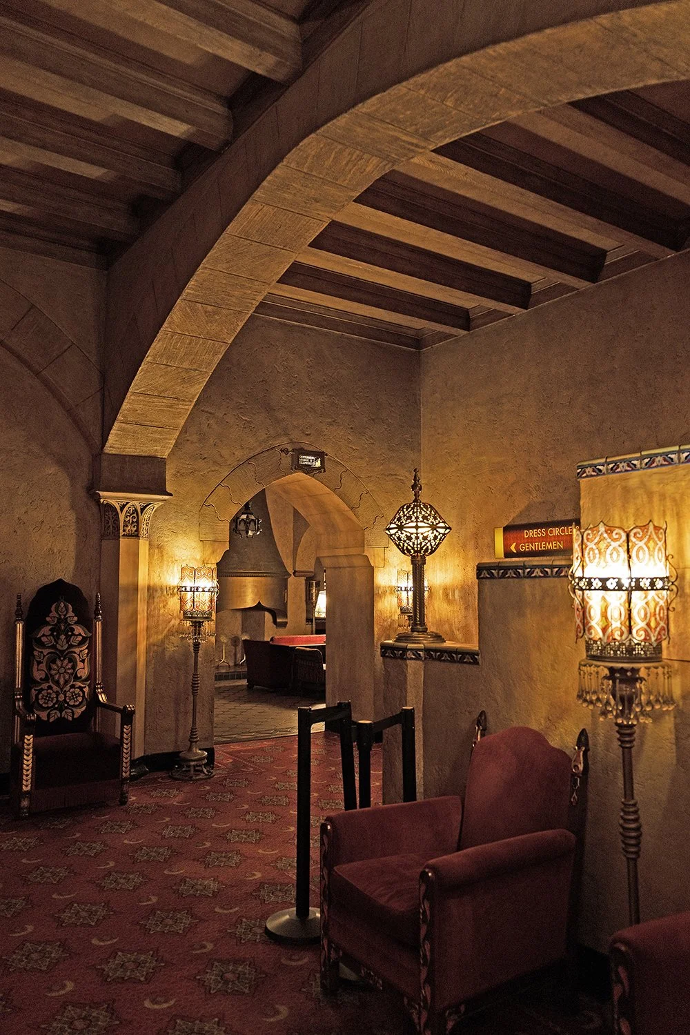 Interior of a lounge area with ornate chairs, decorative lamps, and warm lighting, featuring arched doorways and a patterned carpet. Fox Theatre Atlanta.
