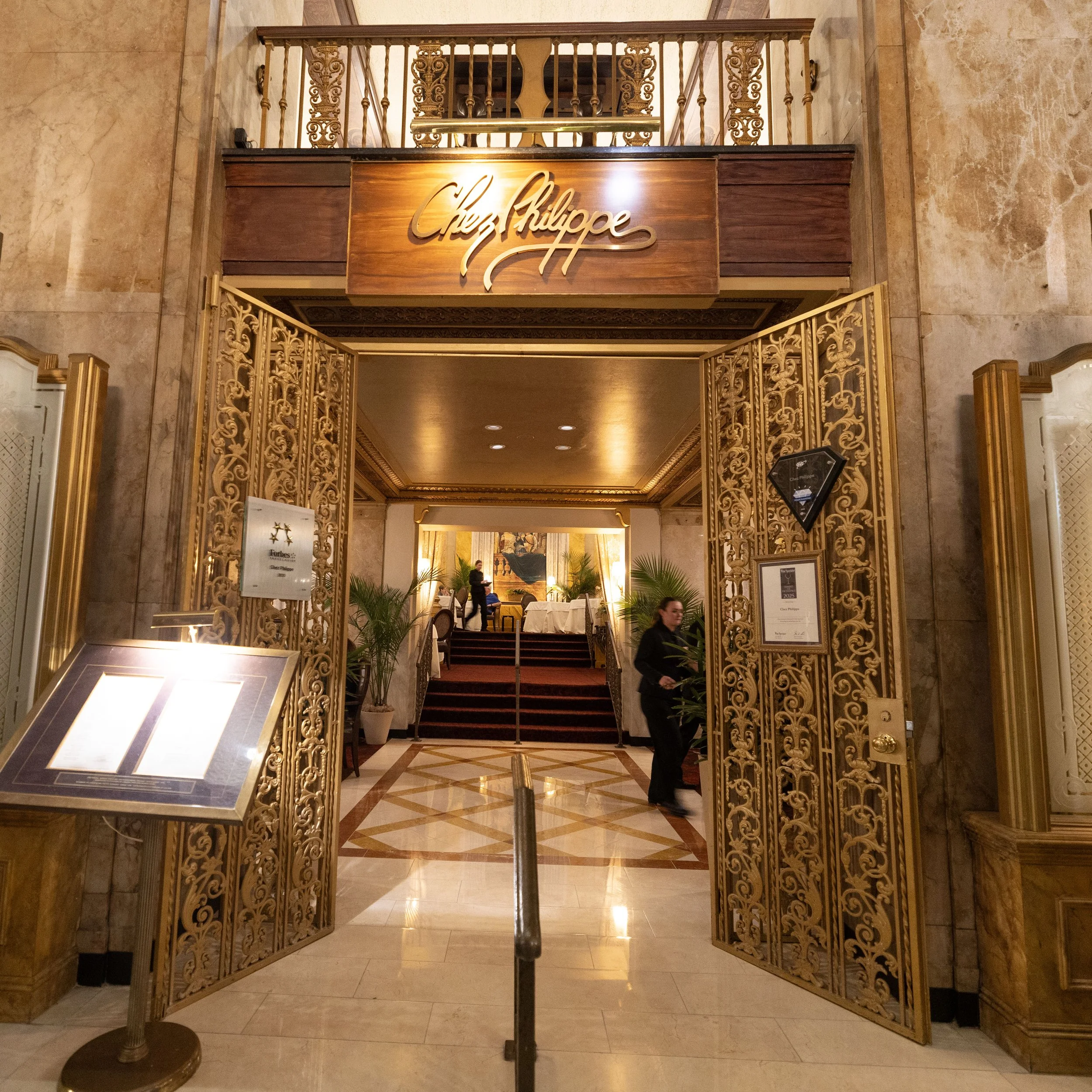 Elegant hotel entrance with ornate gold and wood detailing, featuring a sign that says 'Chez Philippe' above the doorway. Peabody Hotel Memphis.
