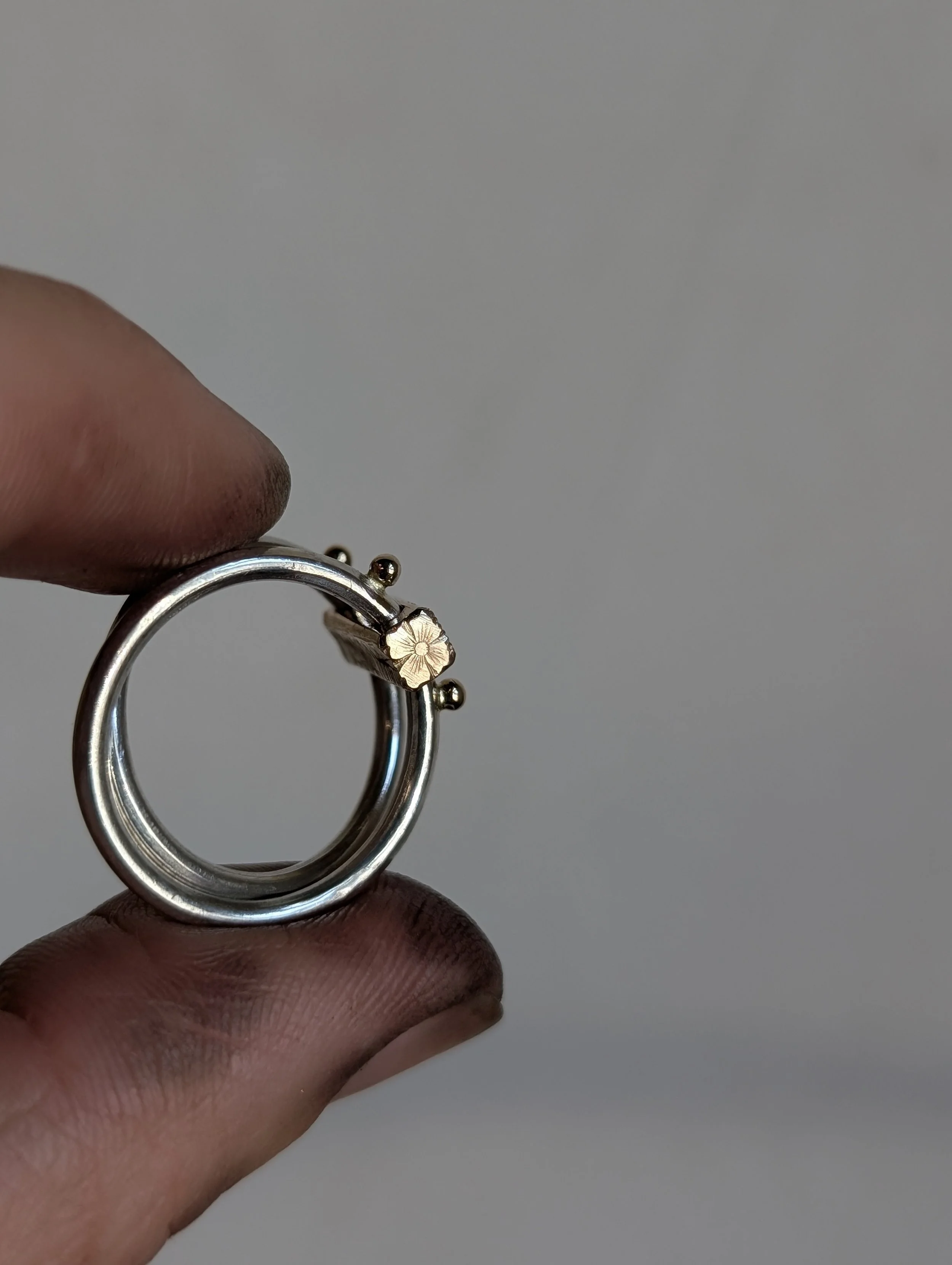 Close-up of a silver ring with a small flower-shaped detail, held between fingers against a plain background.