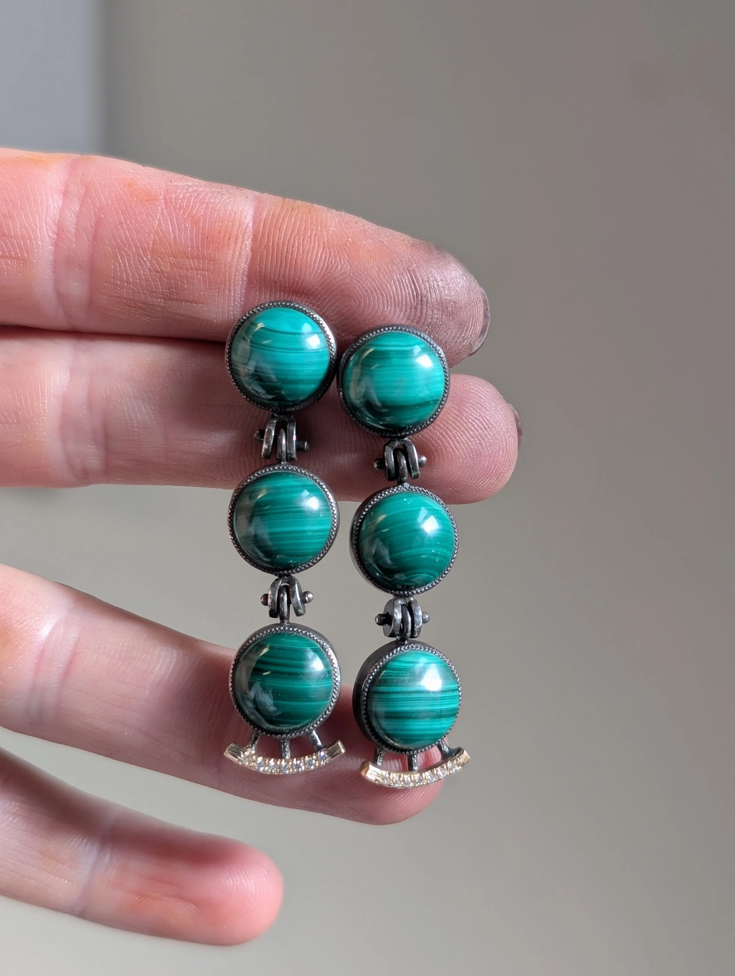 A hand holding a pair of dangling earrings with large, round turquoise stones in silver-colored bezels.