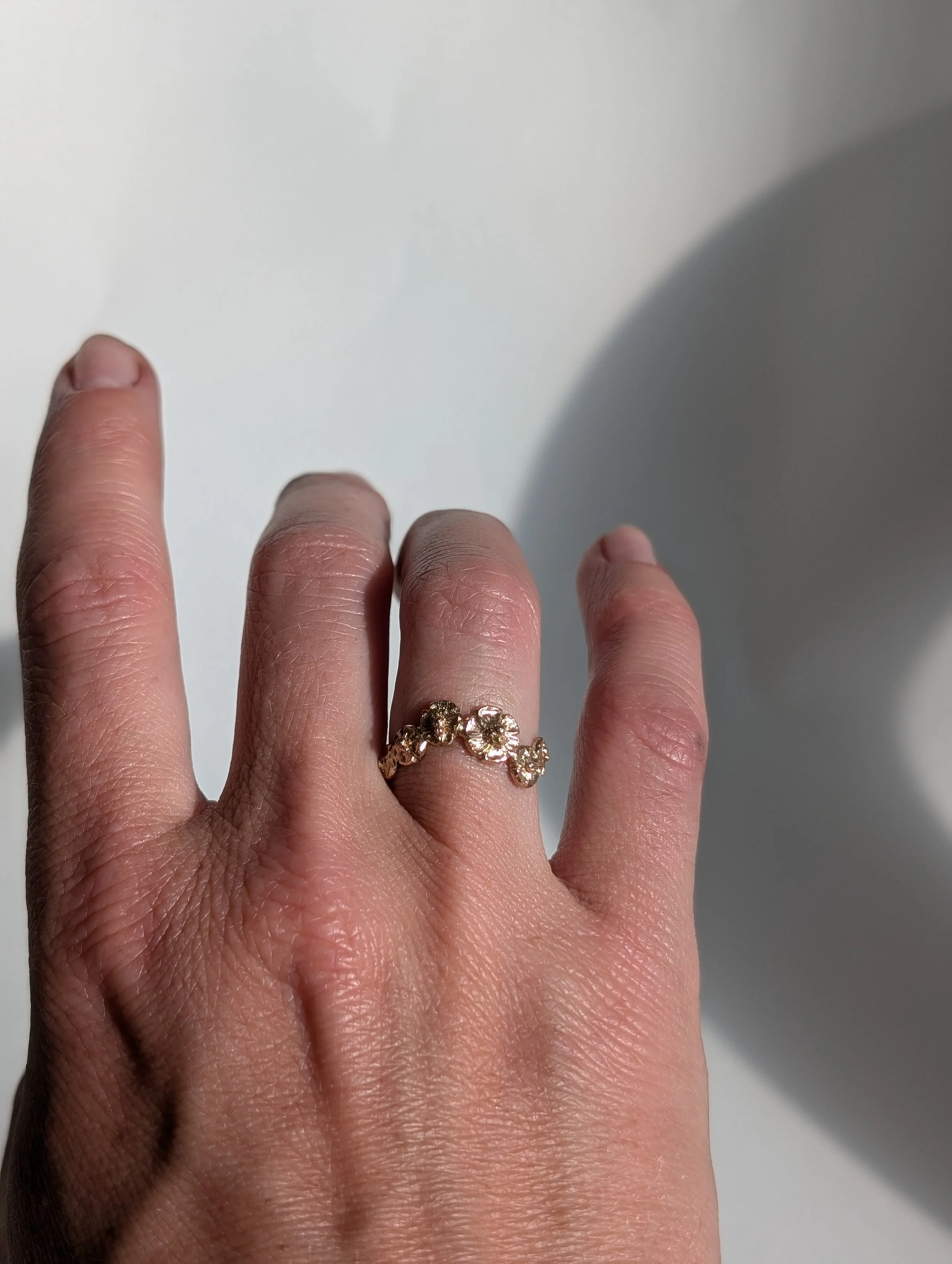 A hand with a gold ring featuring multiple small, round gemstones on the middle finger.