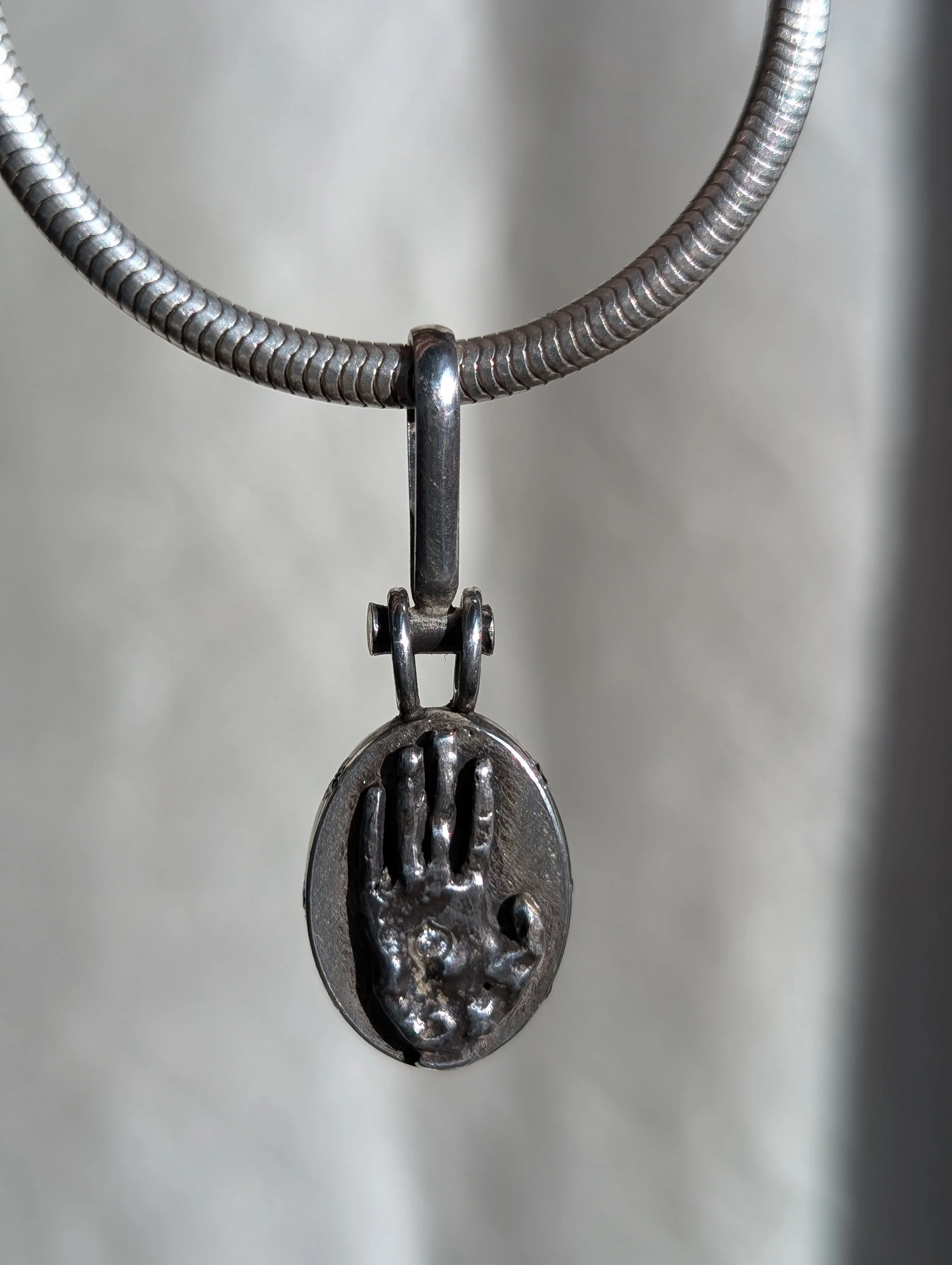Silver necklace with a pendant featuring a raised handprint design.