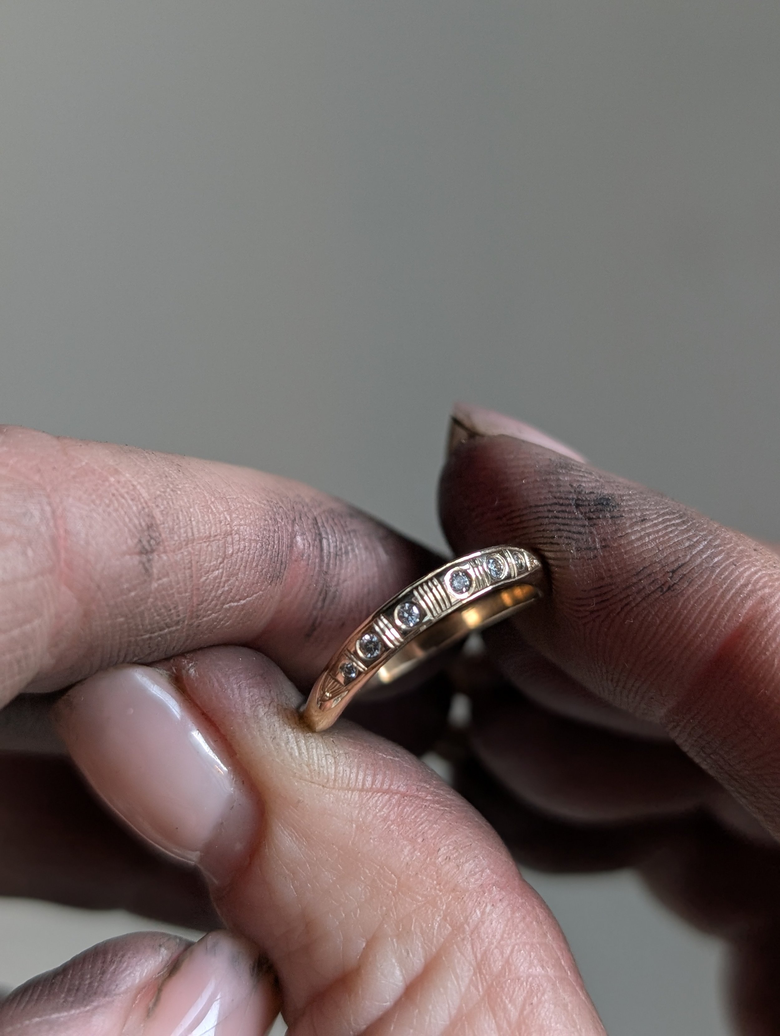 Close-up of two hands holding a gold ring with small diamonds, with dirty fingers and nails.