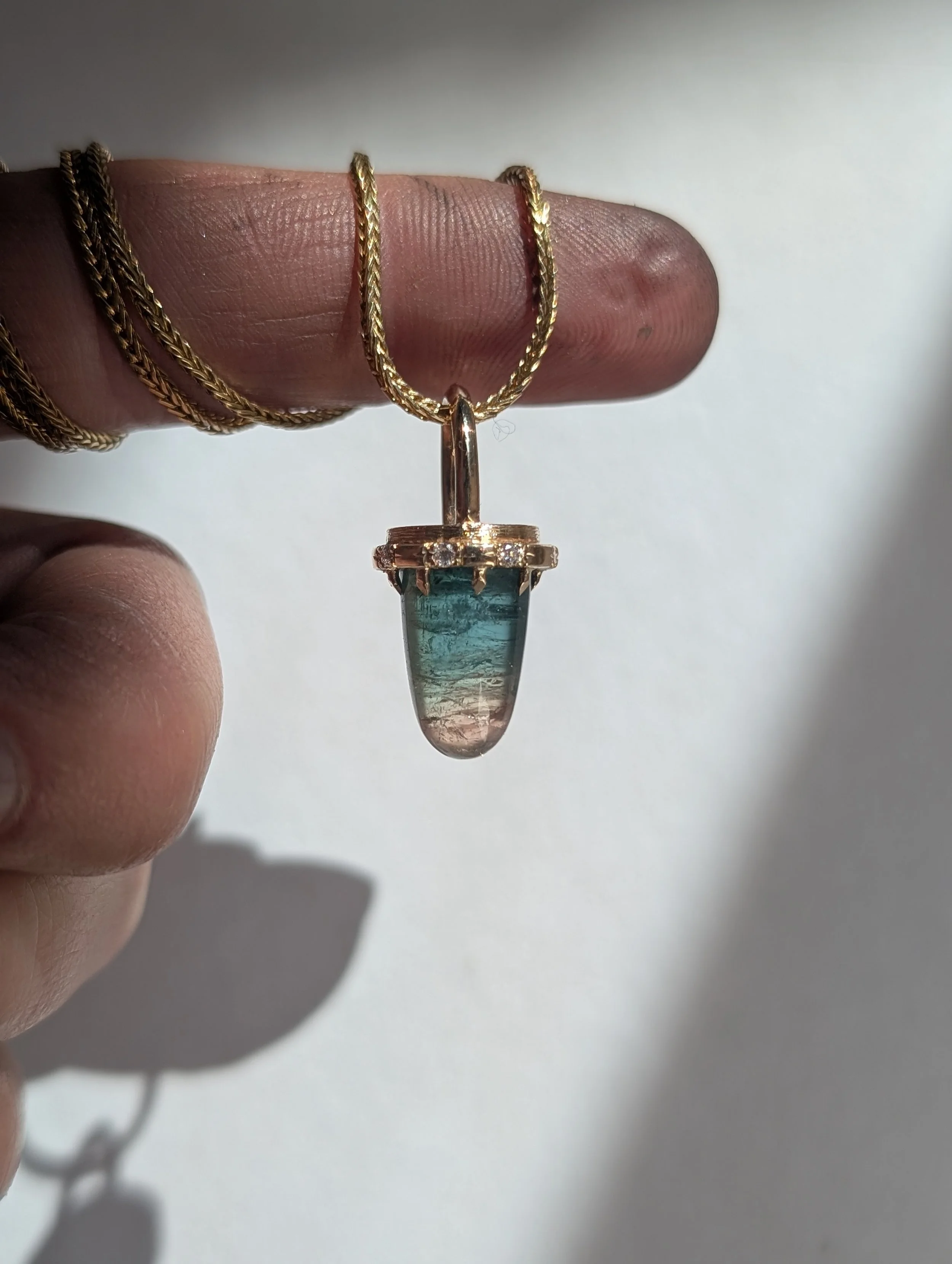 Gold chain with a pendant featuring a multi-colored, tapered glass stone.