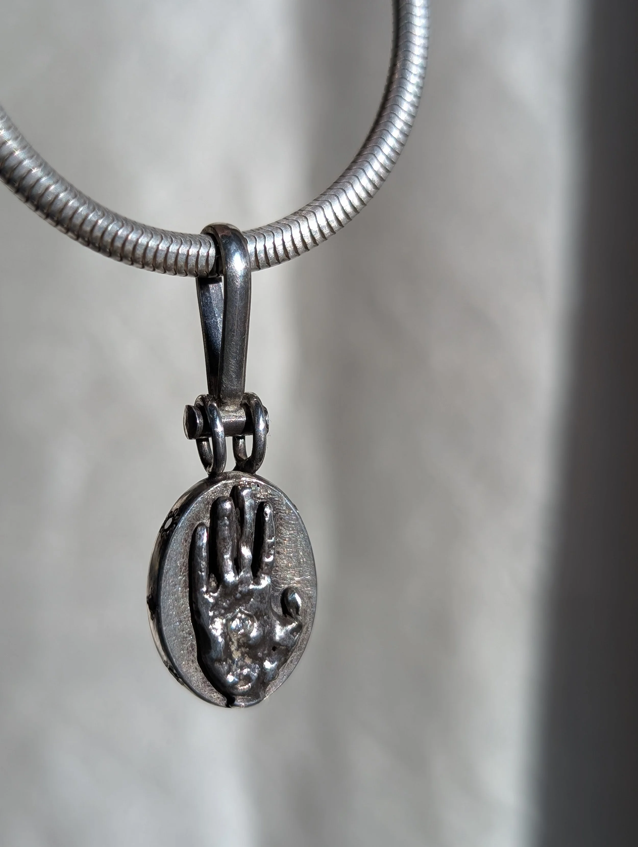A silver necklace with a pendant featuring an engraved handprint.
