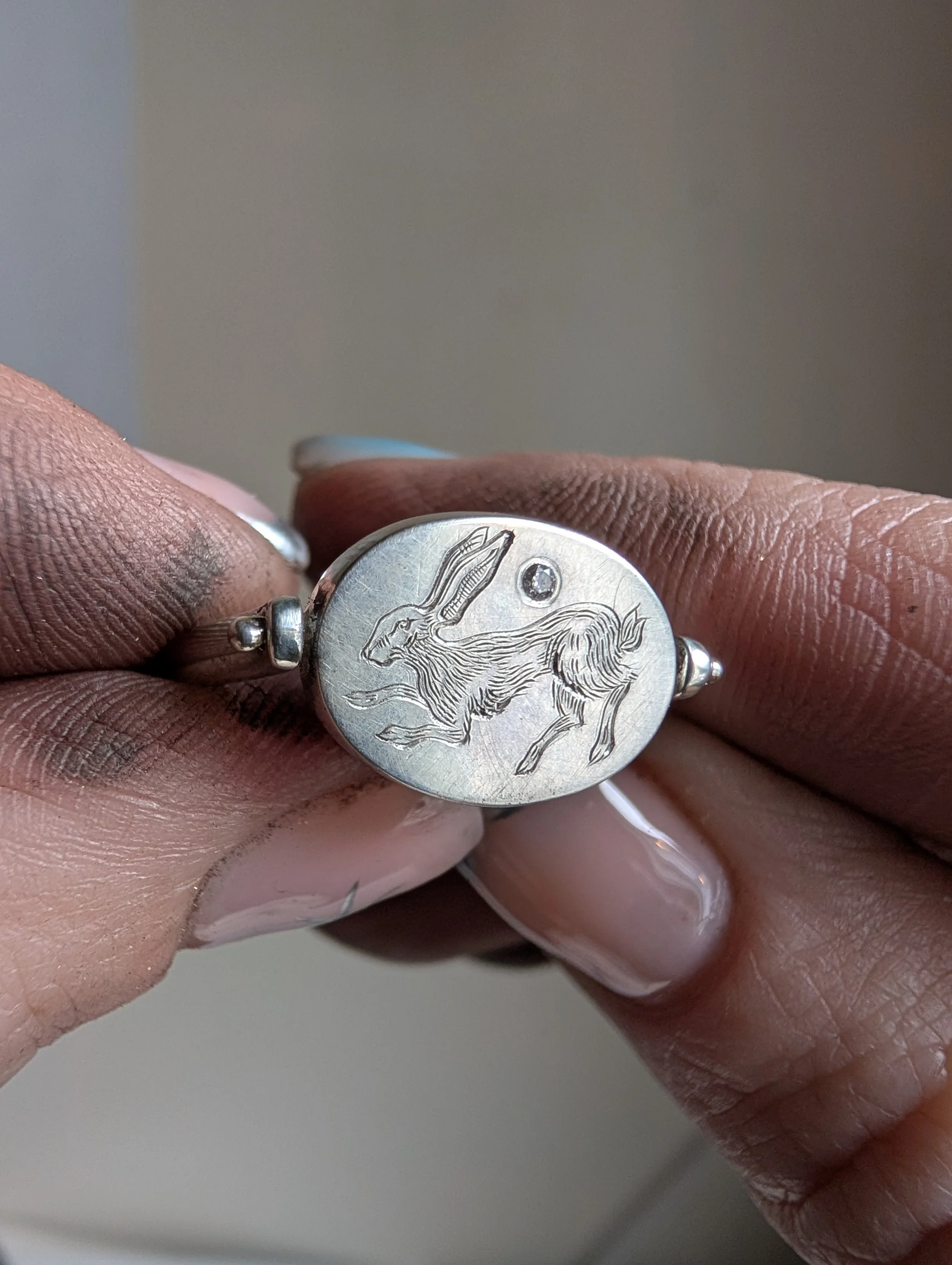 Close-up of a silver ring featuring an engraved rabbit and a small gemstone.
